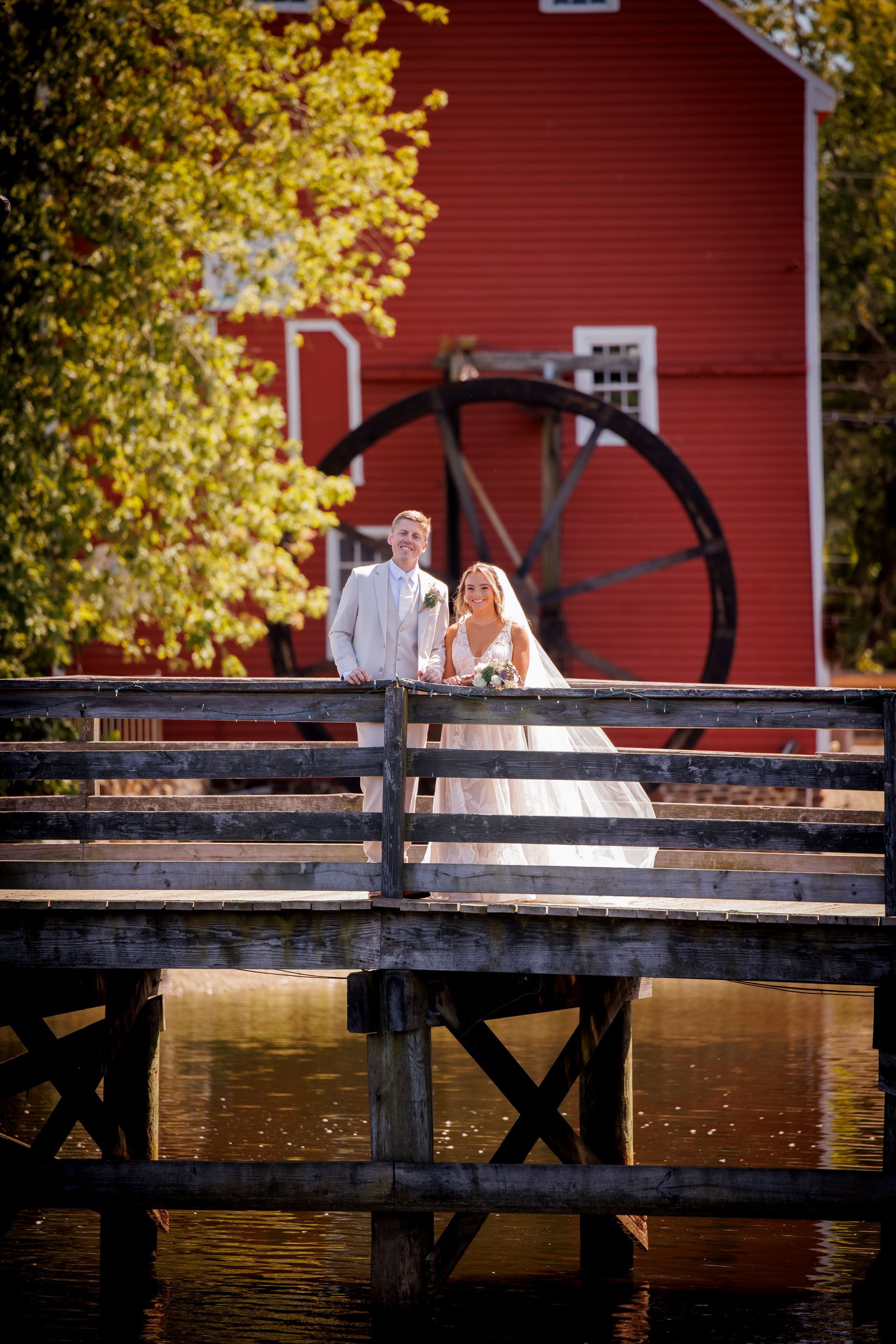Bride and groom on a wooden bridge beside a red mill and water wheel in autumn