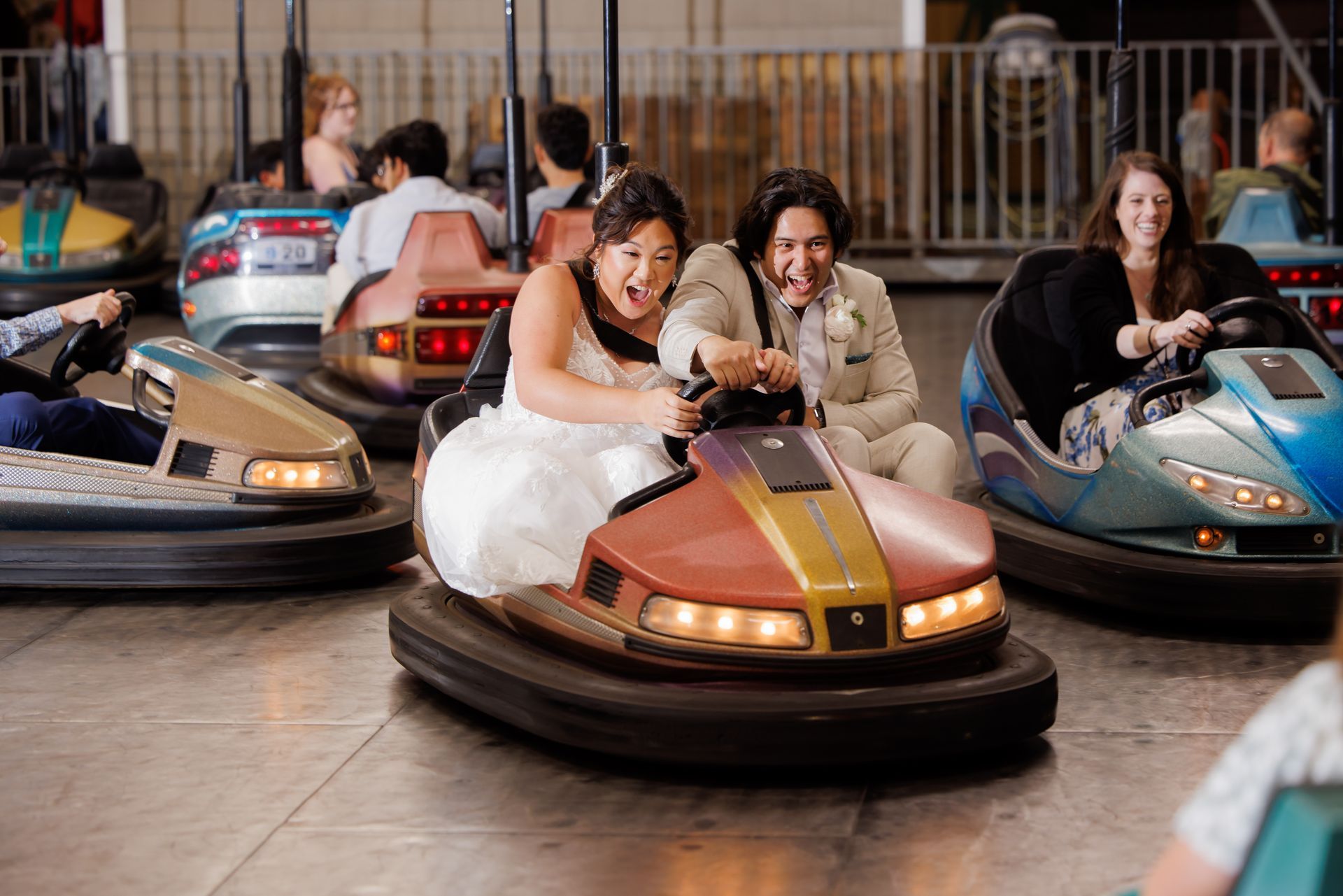 People riding bumper cars indoors, including a white car with a gold stripe in front