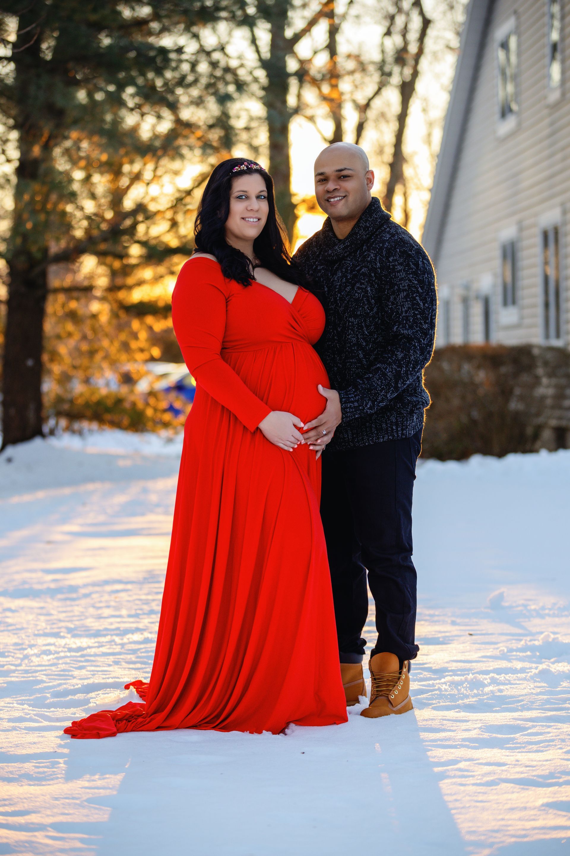 A couple stands together in snow, with the woman in a red dress and the man in a dark patterned shirt.