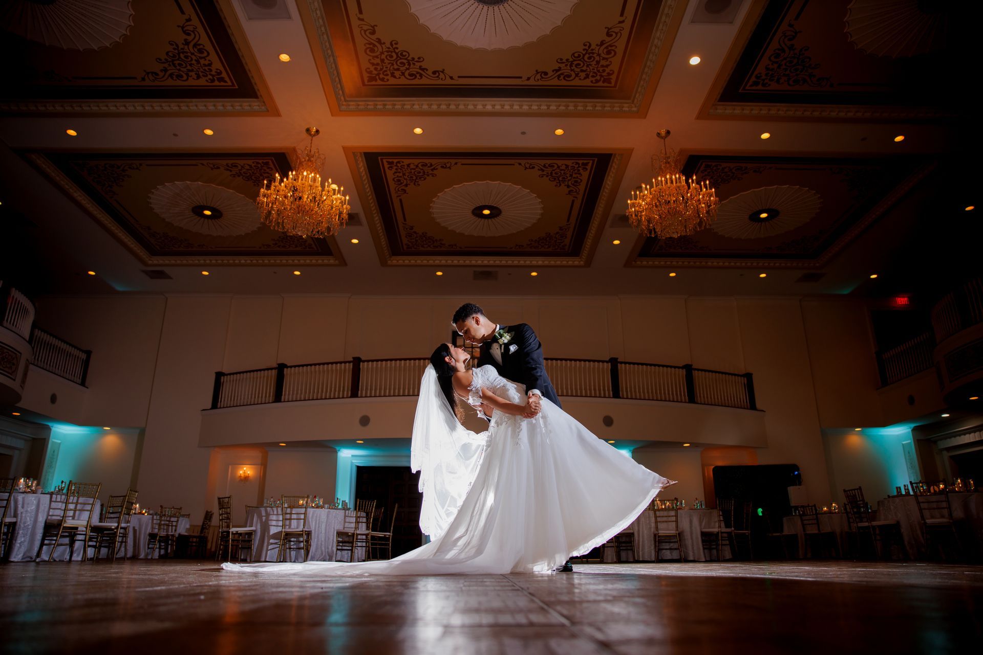 Bride and groom dancing in a grand ballroom under chandeliers, her white dress flowing.