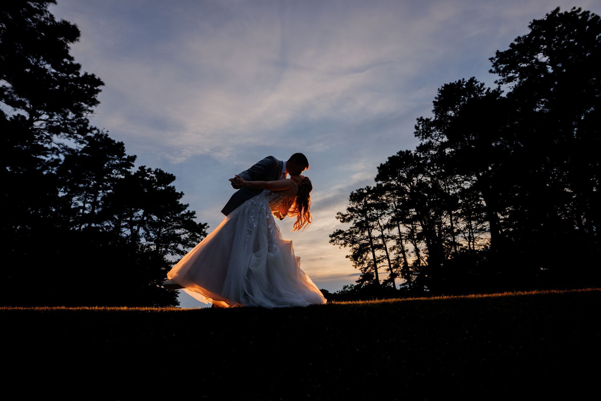 Silhouetted couple in wedding attire embracing at sunset in a wooded clearing