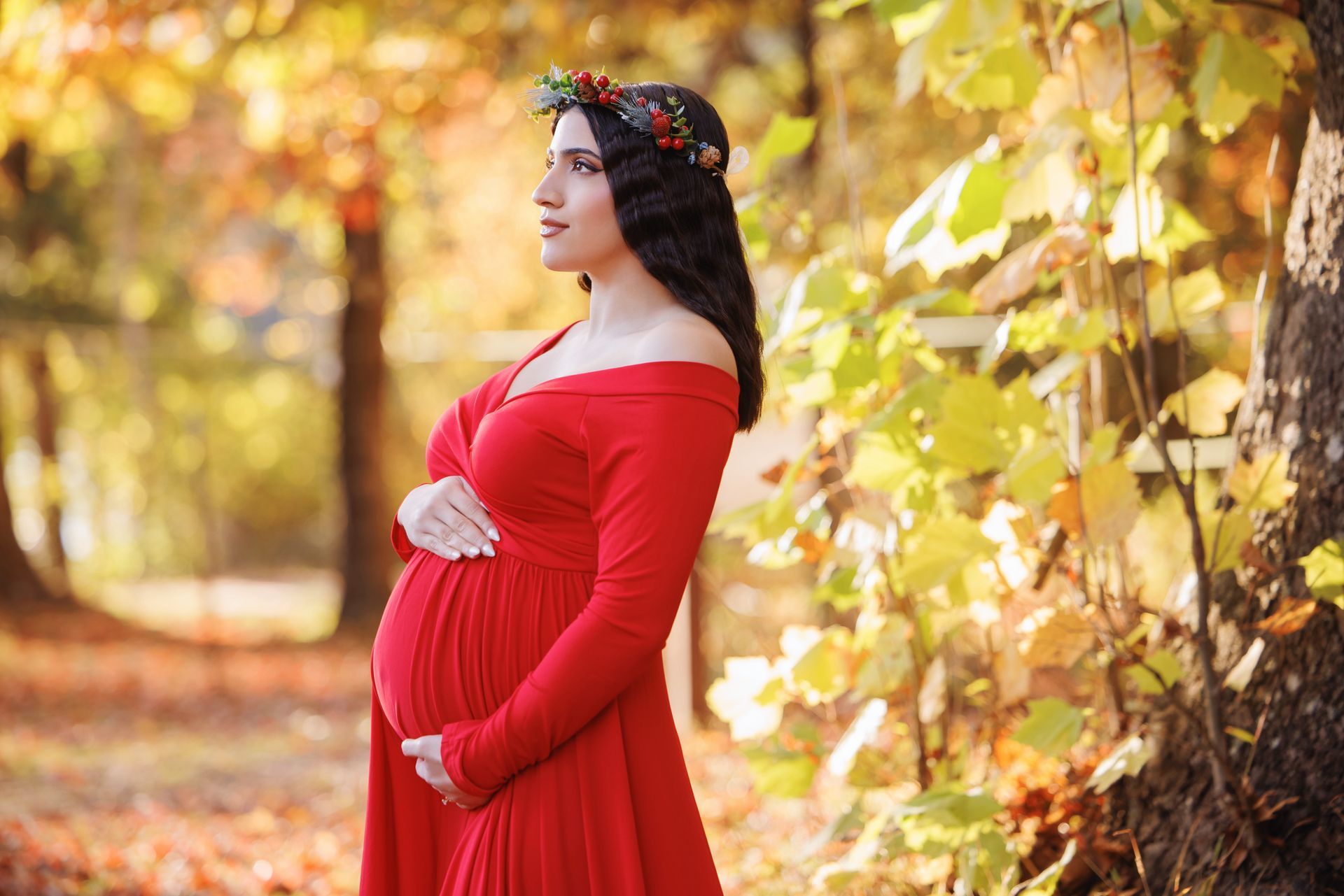 Pregnant woman in a red dress standing outdoors among autumn leaves