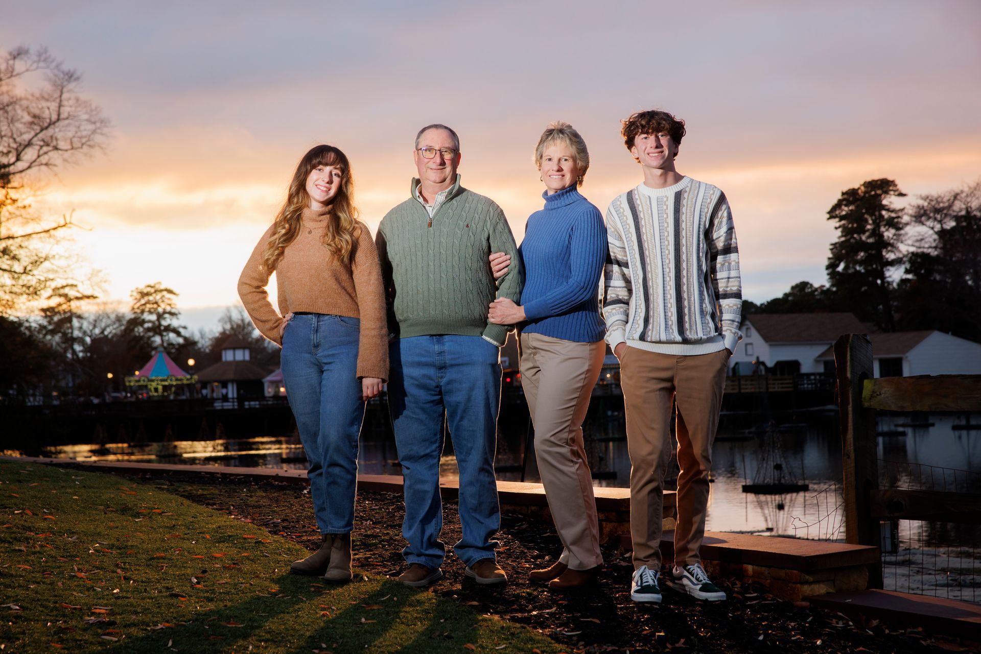 Four people stand outdoors by a canal at sunset, posing under a colorful sky.