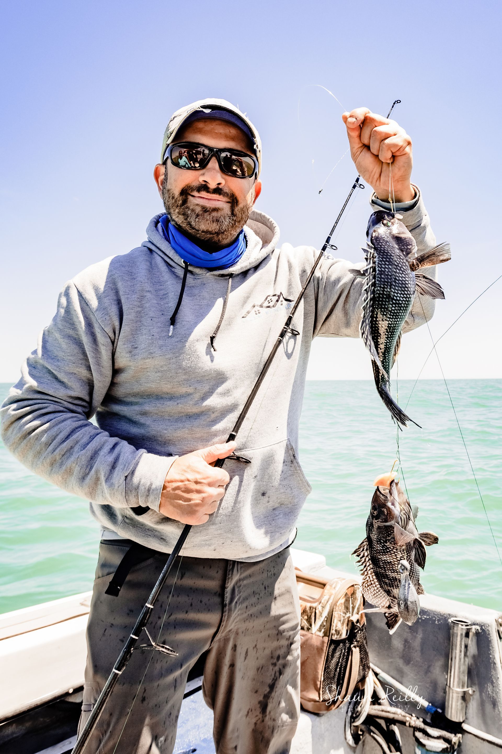 Man on a boat holding a fishing line with a large fish, under a bright blue sky