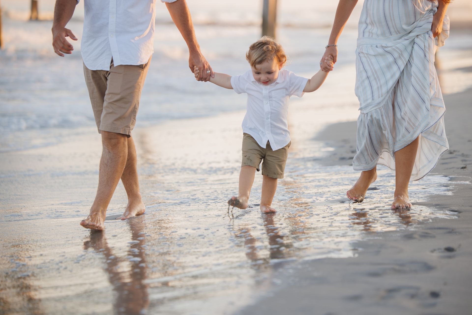 Family holding hands and walking barefoot along the shoreline at the beach