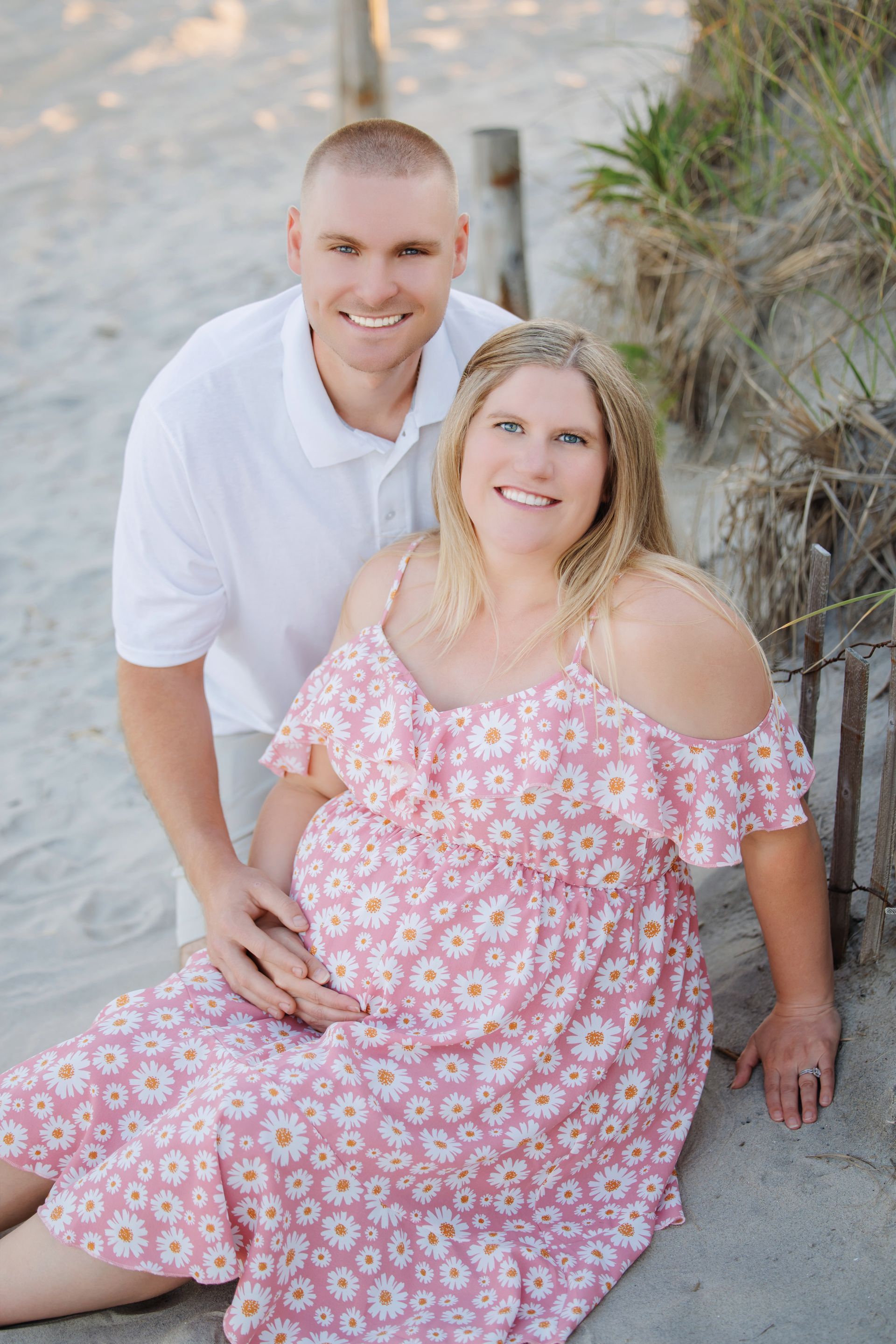 Couple posing outdoors on a sandy path, woman in pink floral dress and man in white shirt