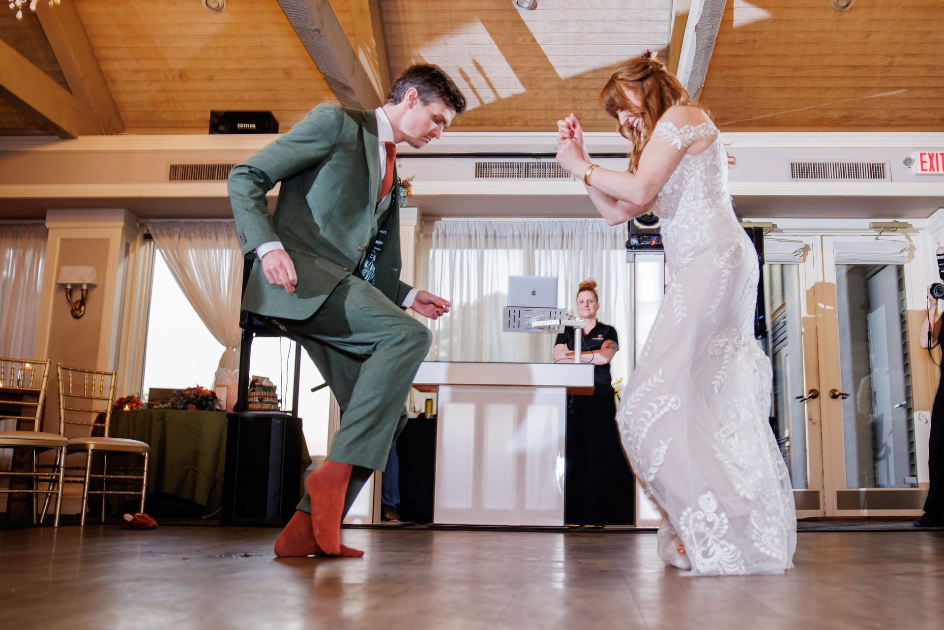 Two people dancing in a bright banquet hall, one in a green suit and one in a white dress.