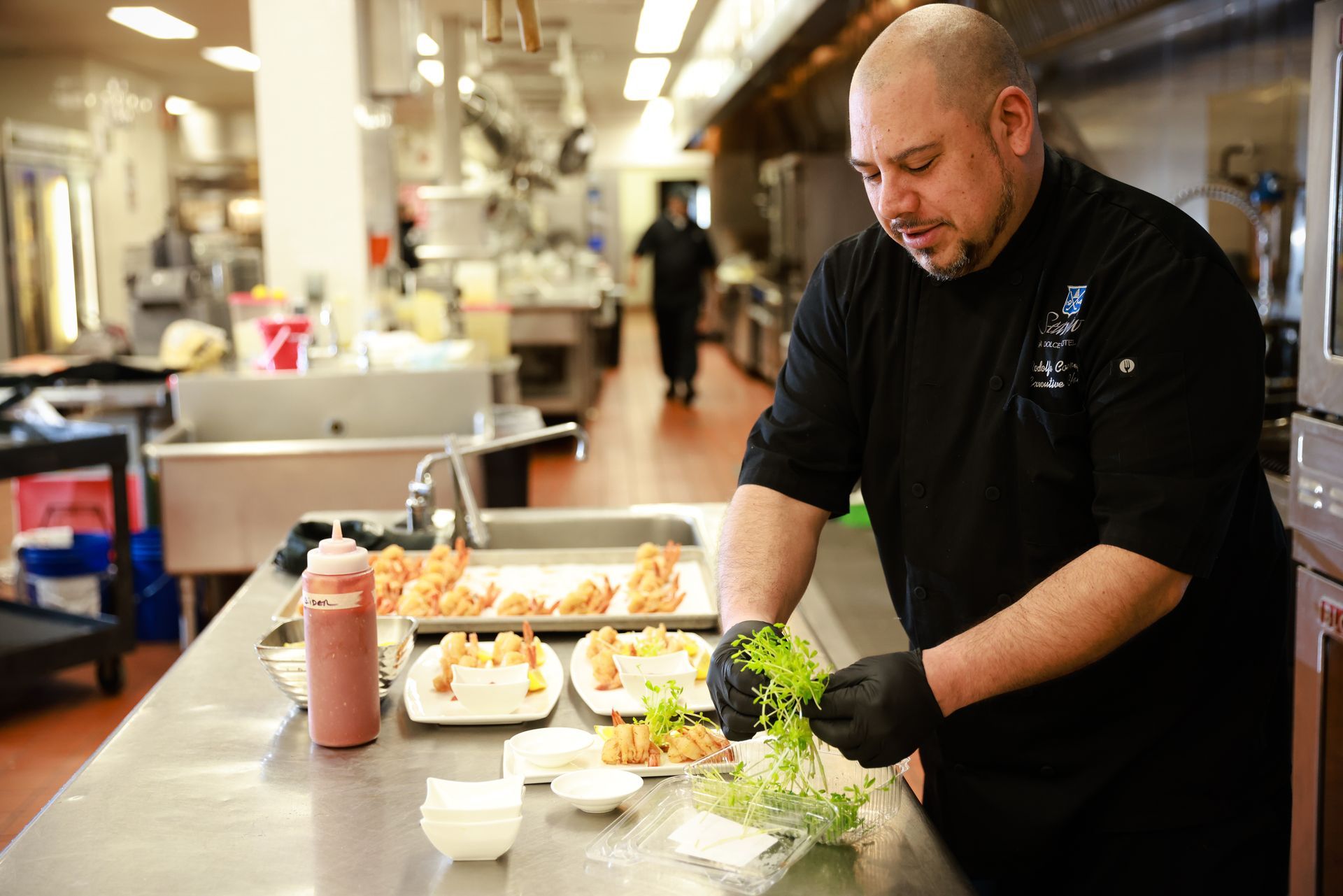 Chef preparing food on a stainless-steel counter in a busy commercial kitchen.