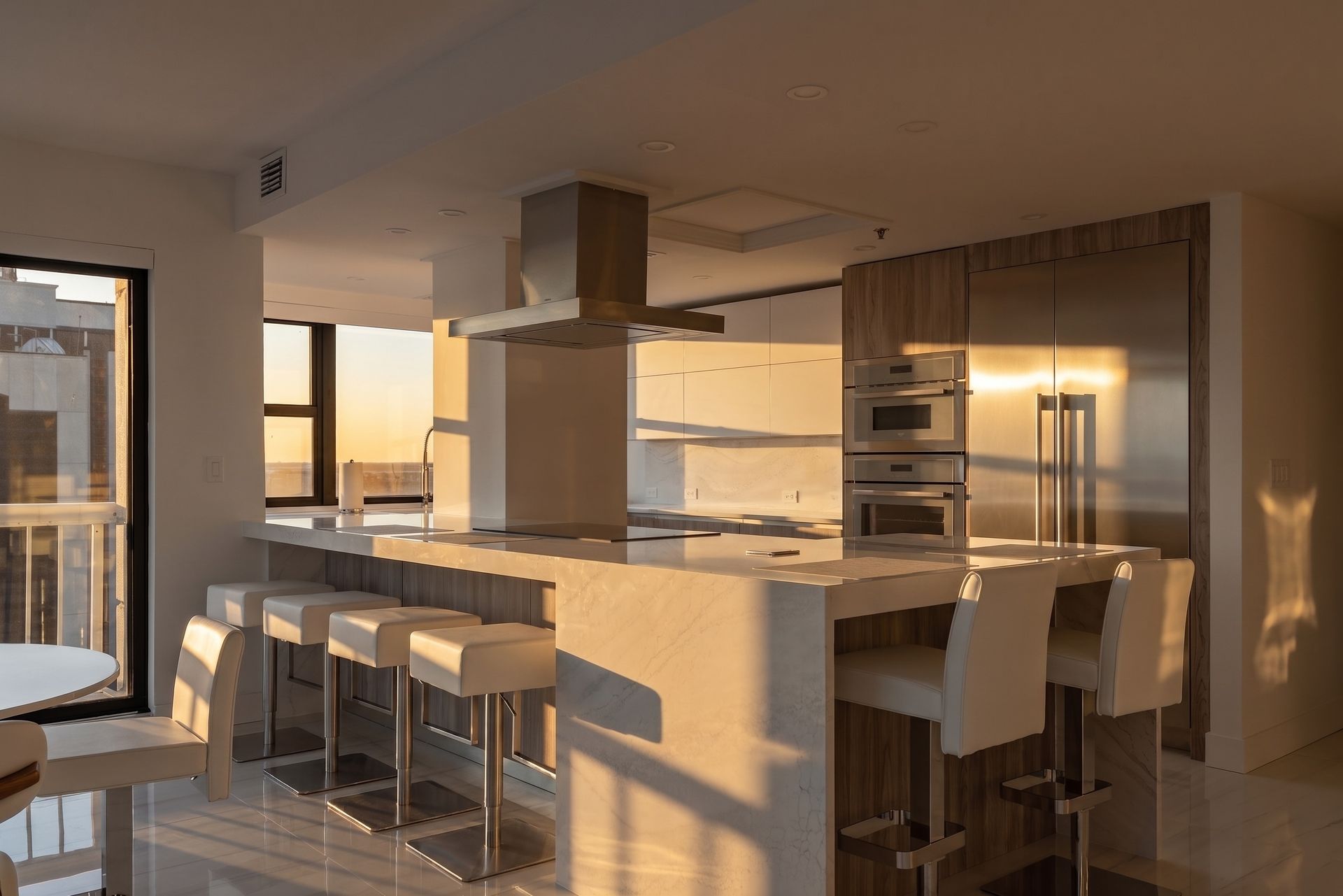 Modern kitchen with island seating, stainless appliances, and warm sunset light through large windows