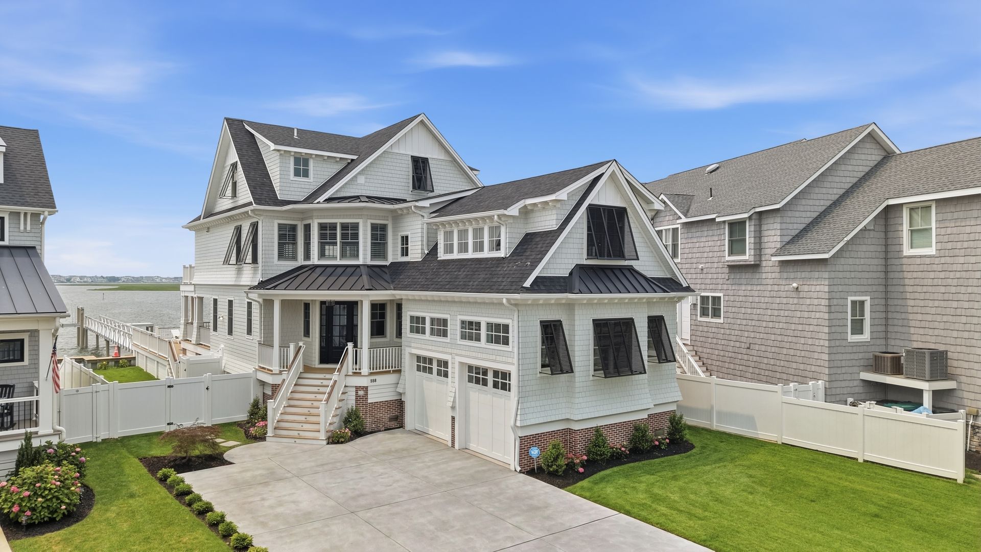 White coastal-style house with gray shingles, front porch, driveway, and fenced yard under a blue sky