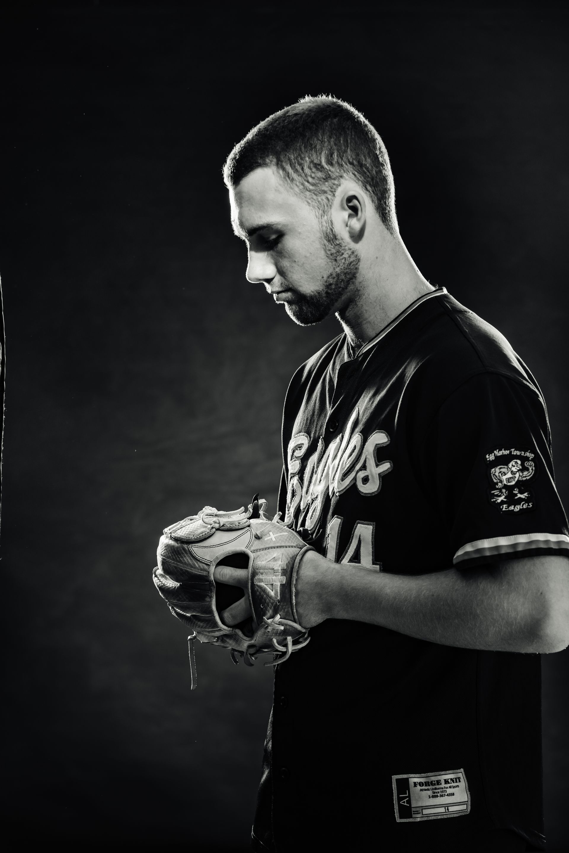 Black-and-white portrait of a baseball player in a dark jersey, holding and looking down at a glove.