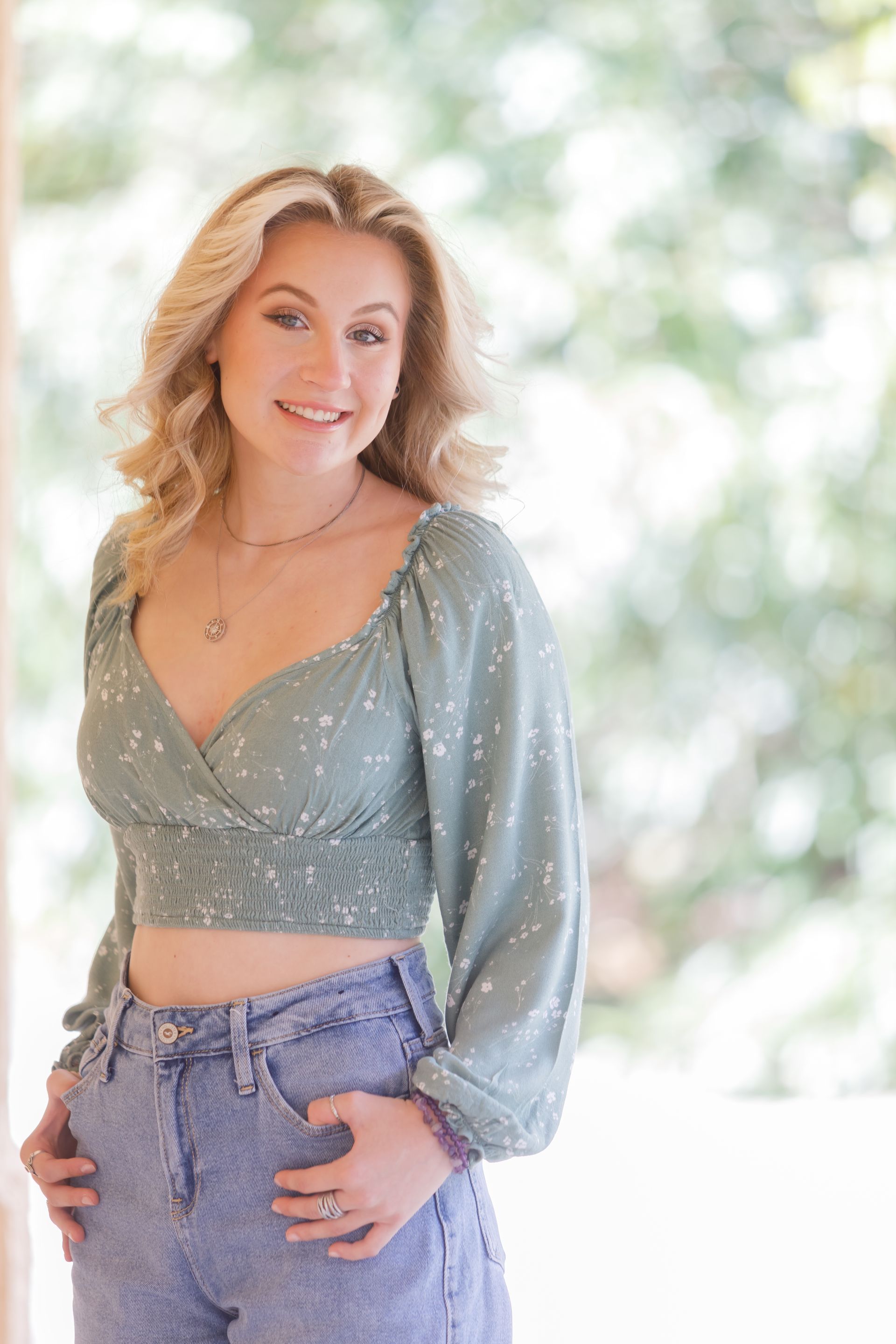 Woman in a green blouse and purple pants posing against a bright blurred background