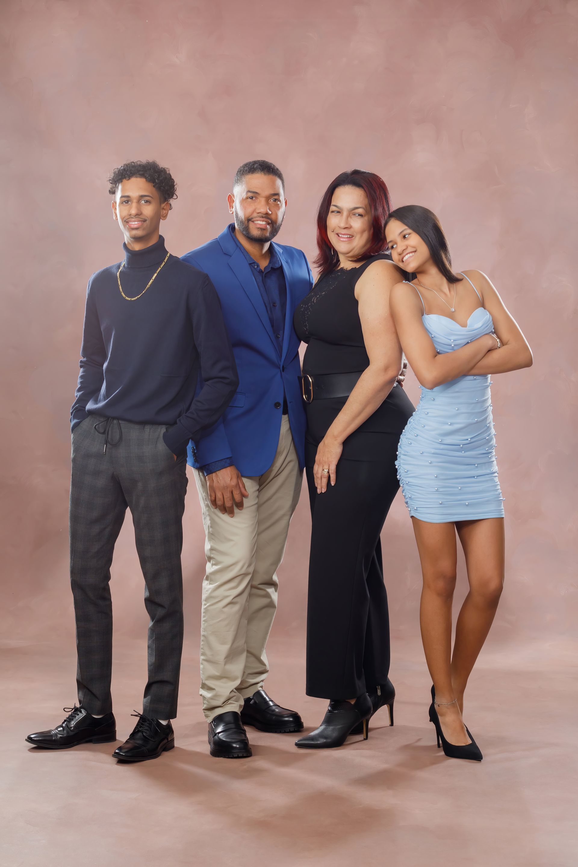 Four people posing against a pink studio backdrop, dressed in blue, black, and beige outfits.