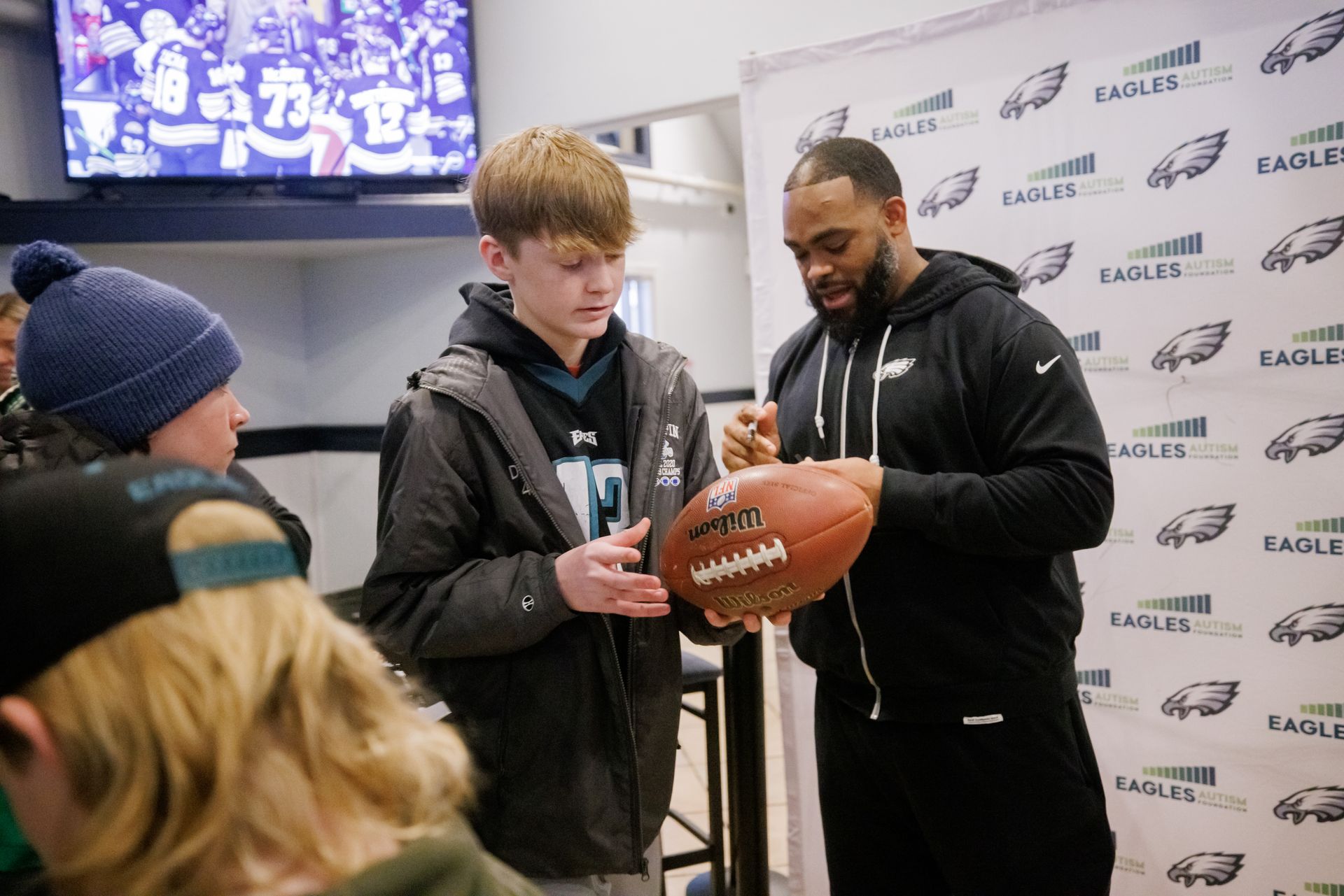 Two men signing a football for a fan at a sports event booth