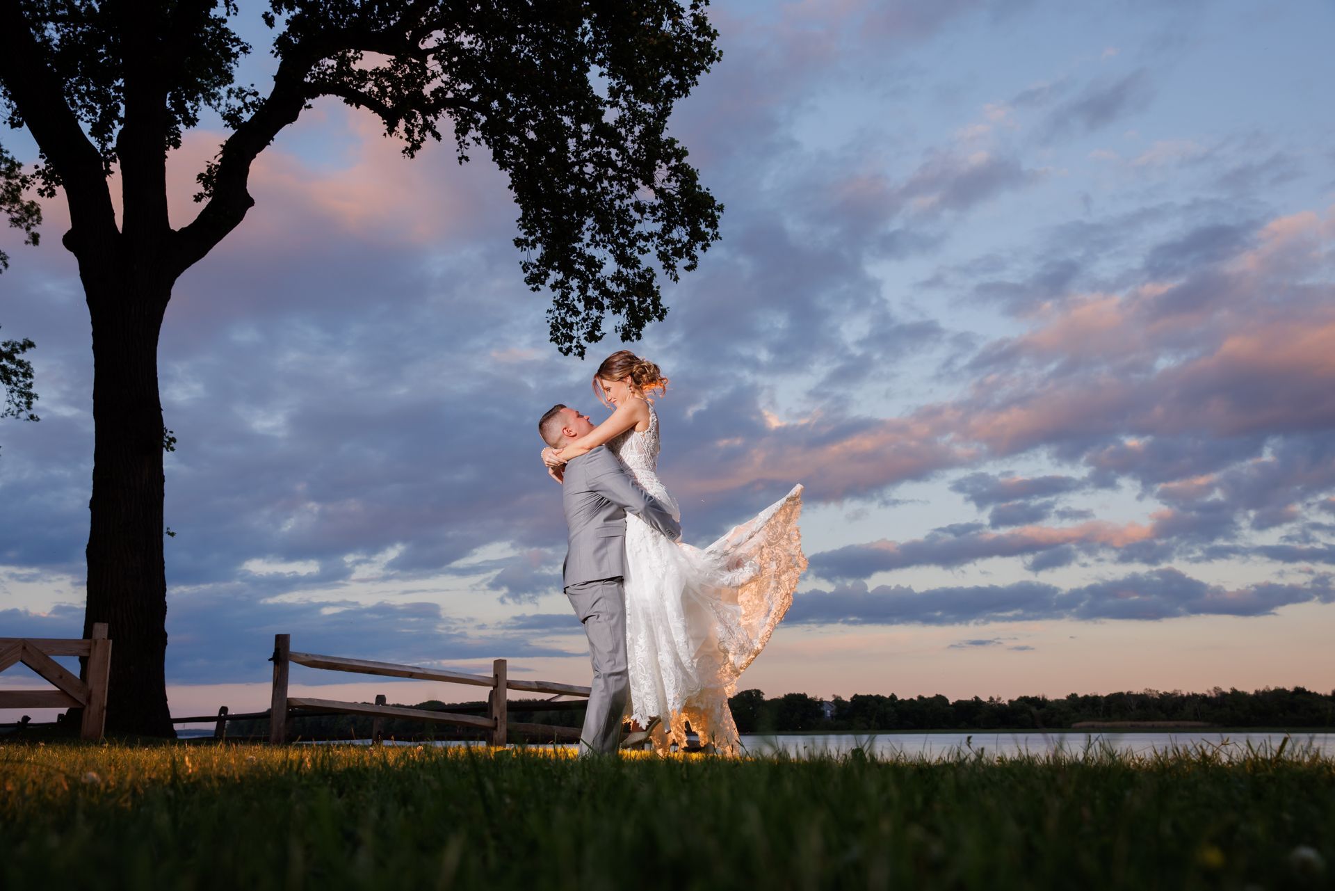 Couple embracing in wedding attire at sunset in a grassy field under a colorful sky