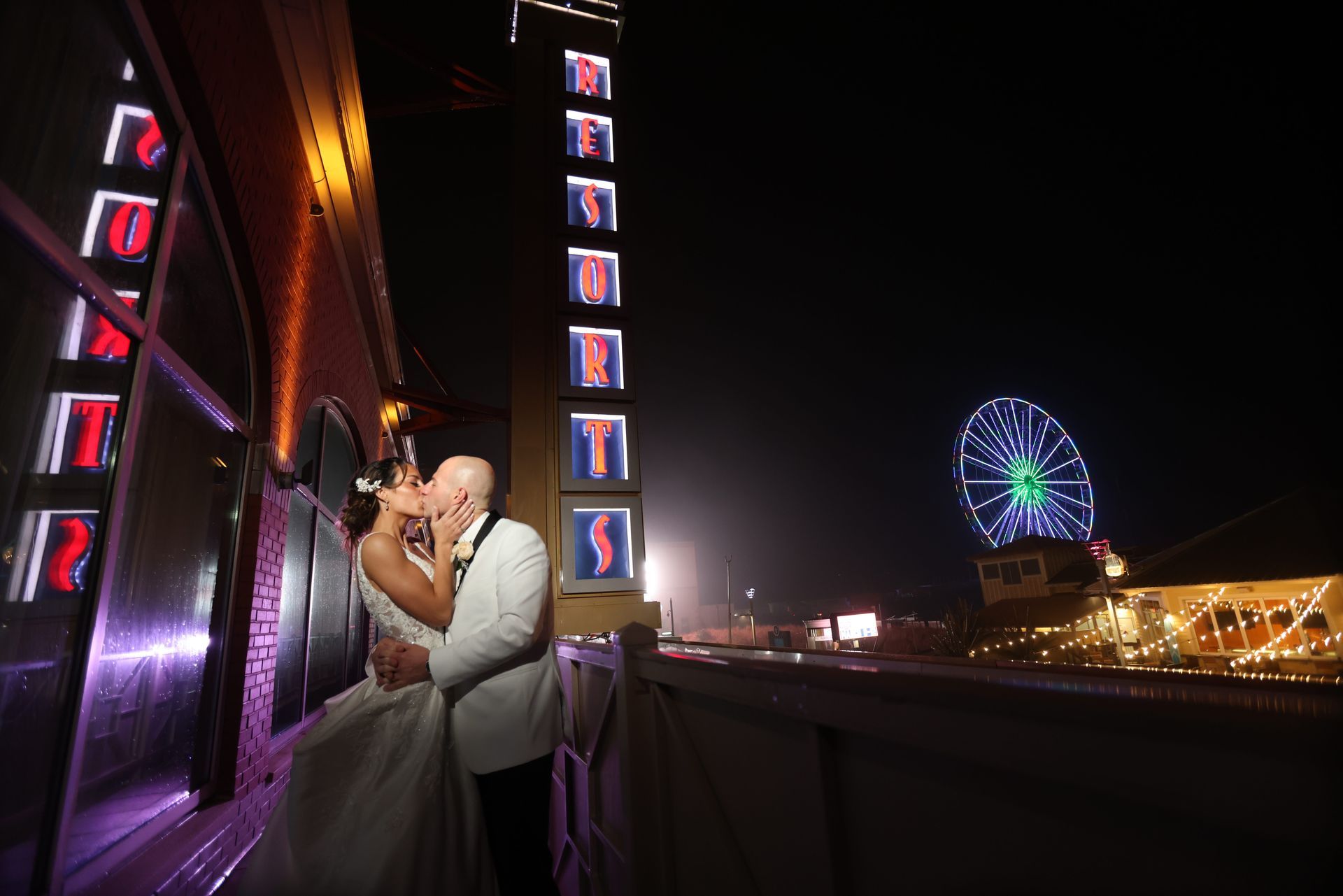 Couple embracing on a neon-lit balcony at night, with a Ferris wheel glowing in the background.