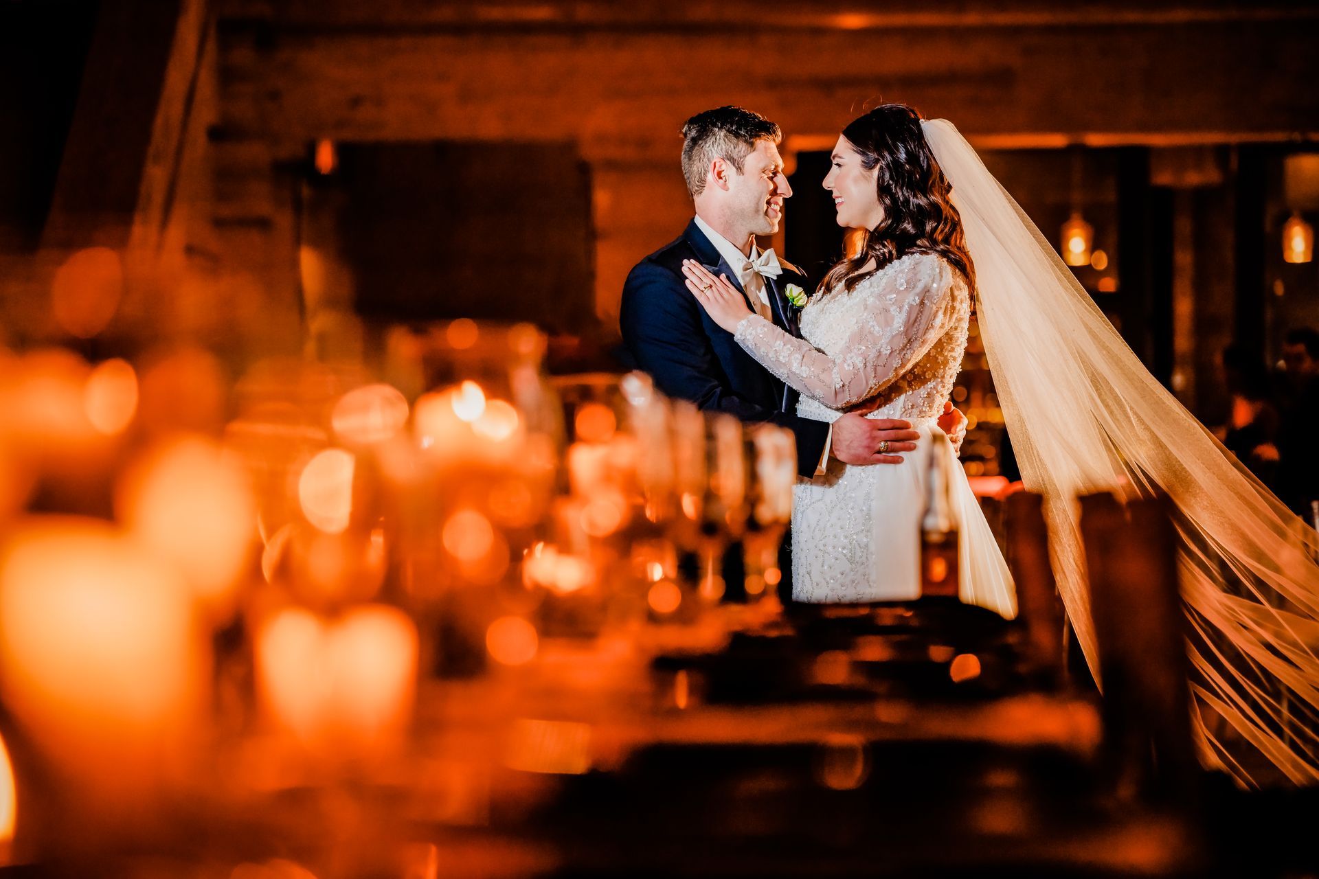 Couple dancing at a warmly lit wedding reception with candles glowing in the foreground