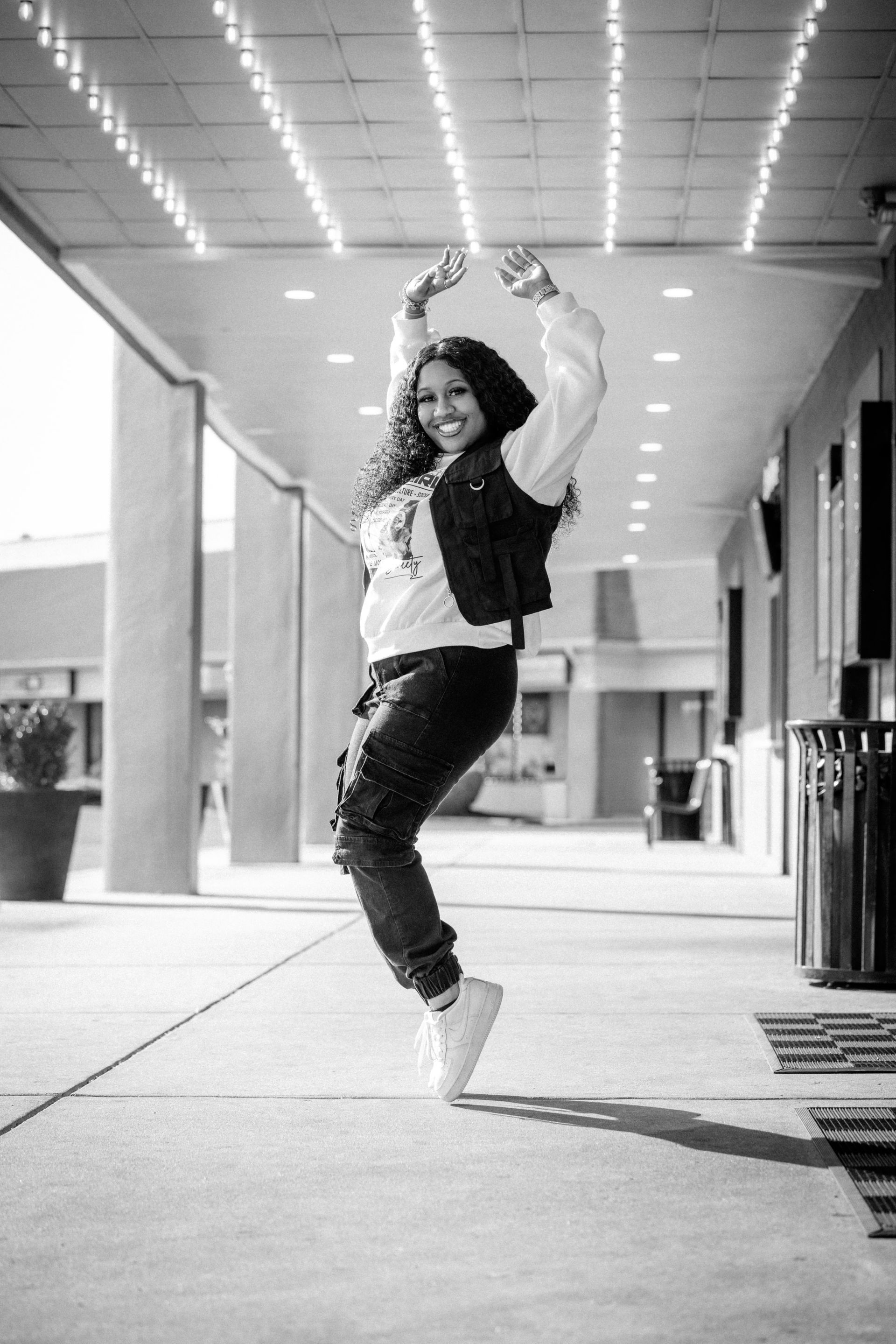 Person dancing under a covered walkway, arms raised and smiling.