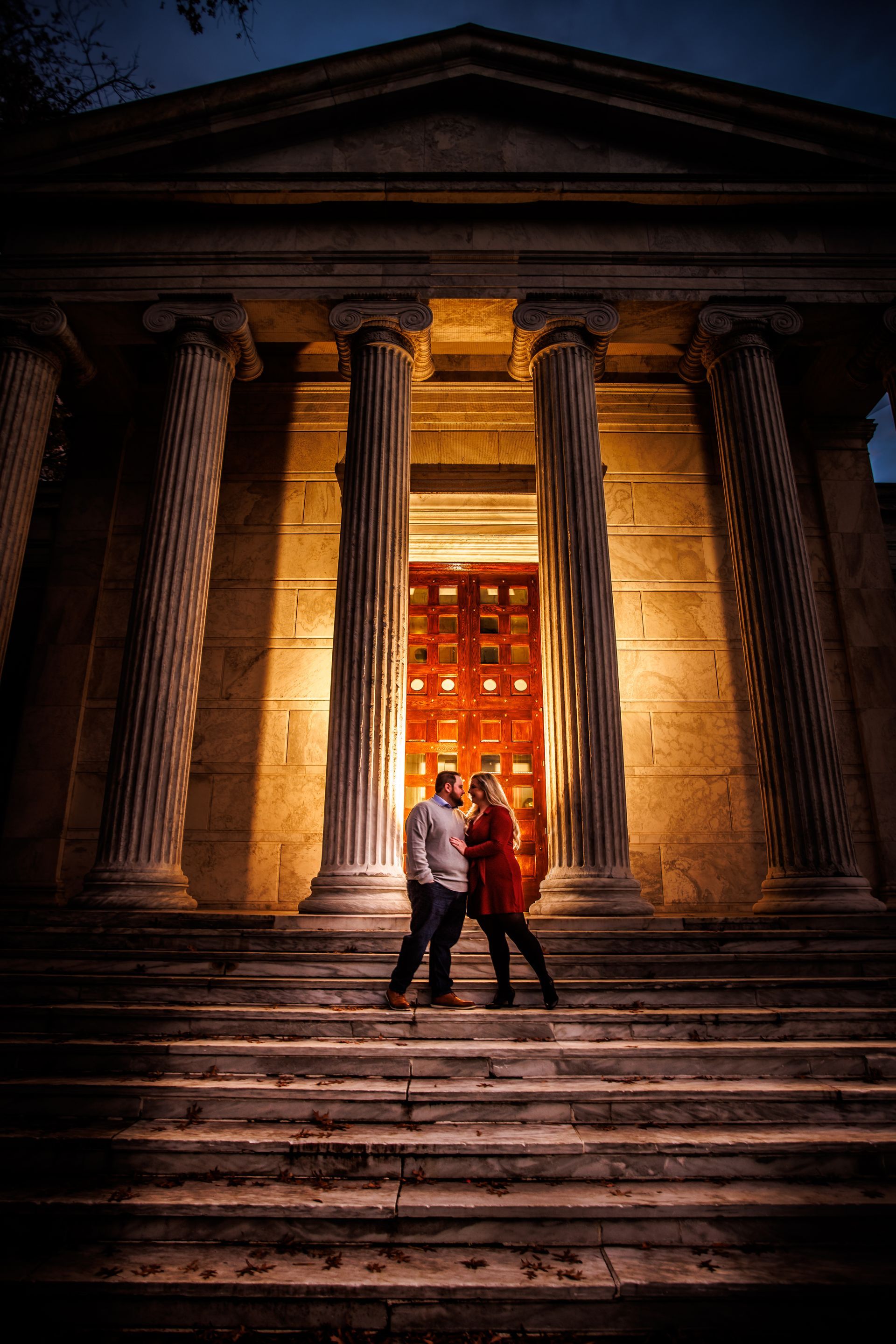 Two people walking up stone steps toward a lit classical building at night
