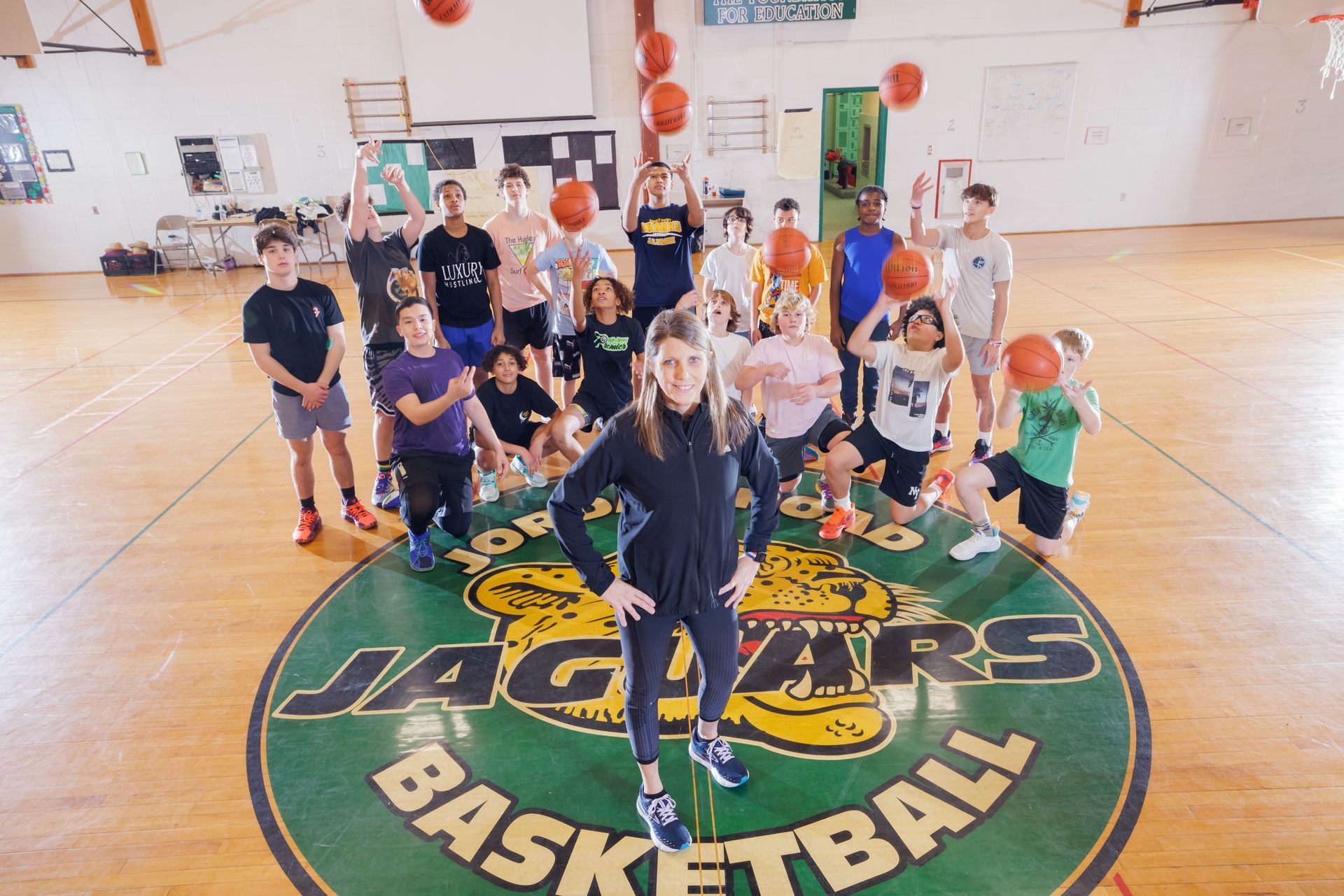 Group of students on a basketball court with a large Jaguars logo, posing with orange basketballs