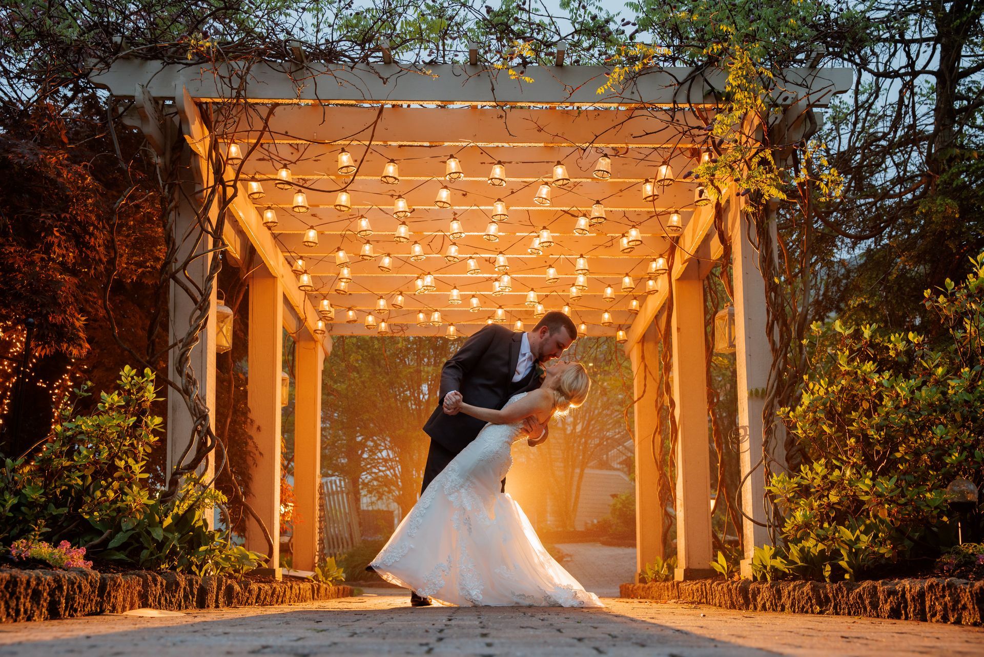Bride and groom dancing under a glowing wooden pergola at dusk