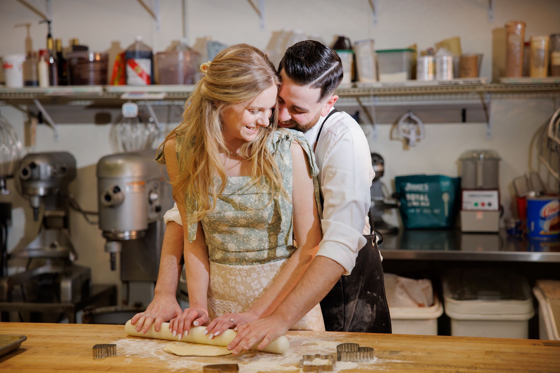 Two people baking together in a kitchen, rolling dough on a wooden counter and smiling.
