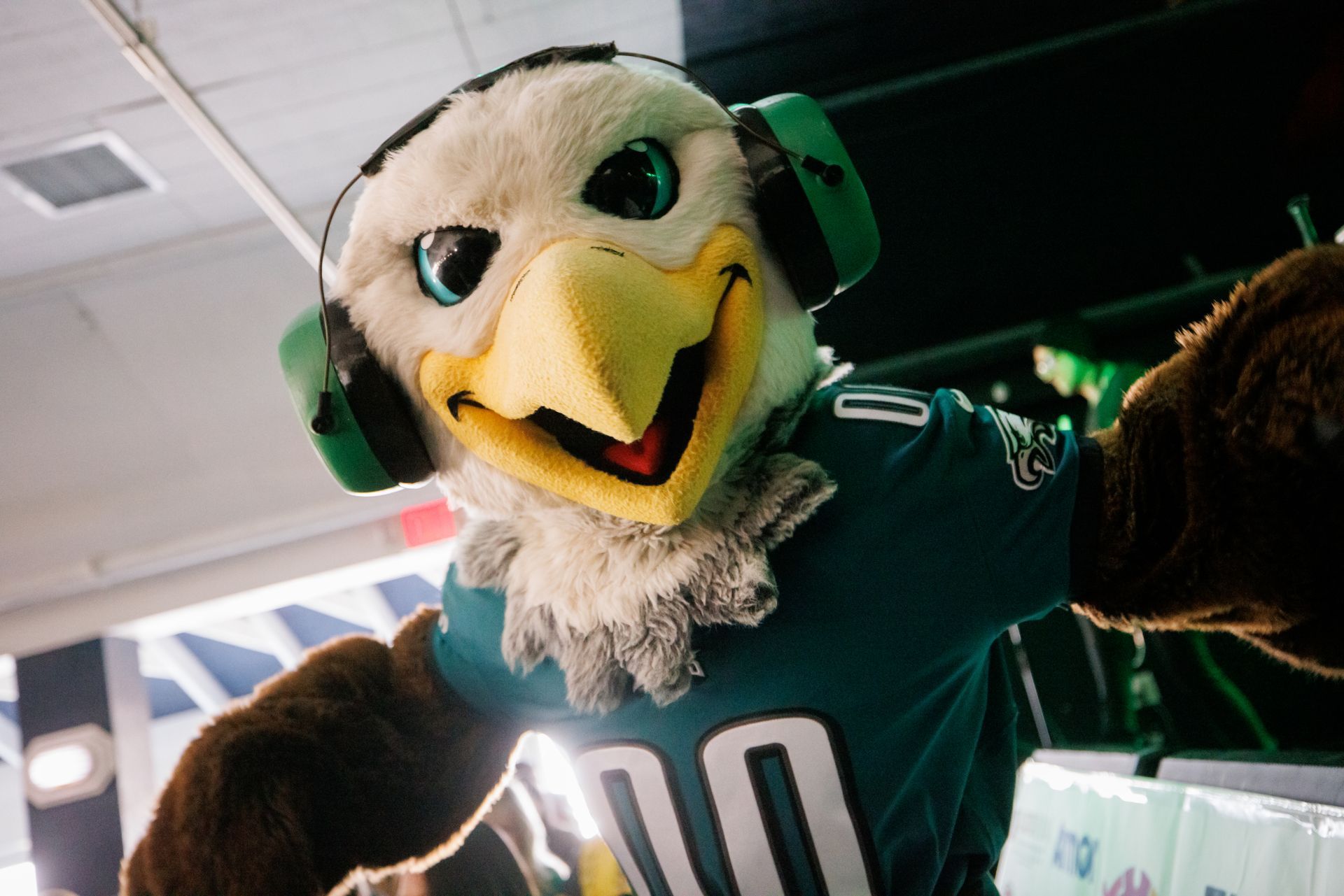 Green eagle mascot in a sports jersey, smiling with wings raised indoors