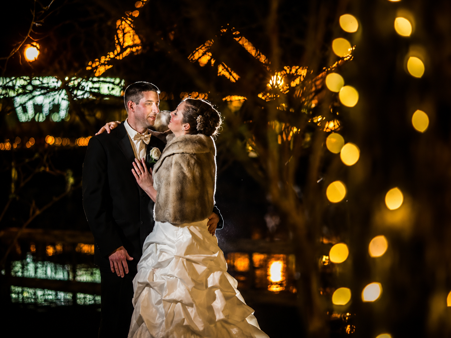Bride and groom embracing at night with warm city lights bokeh in the background