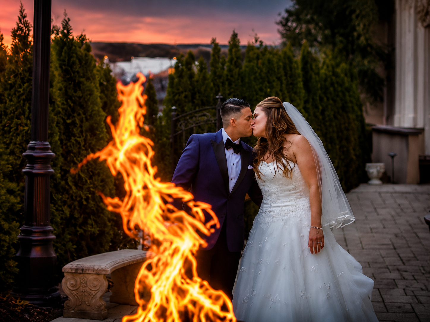 Bride and groom kissing beside a large fire at an outdoor wedding reception