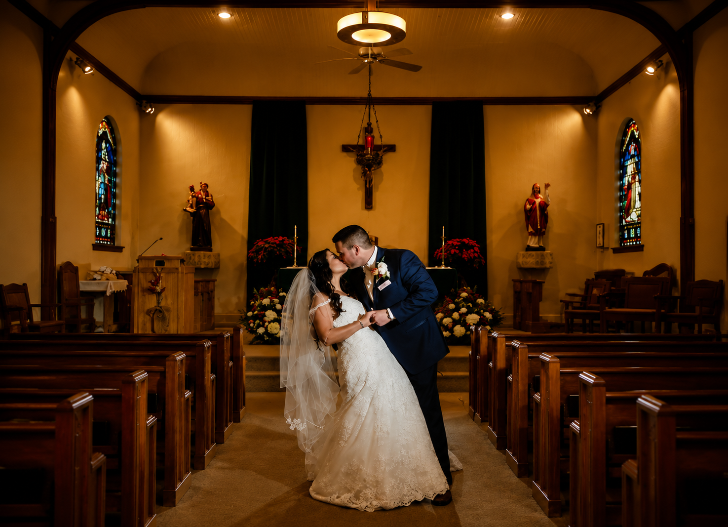 Bride and groom kiss in a church aisle, framed by pews and warm golden lighting.