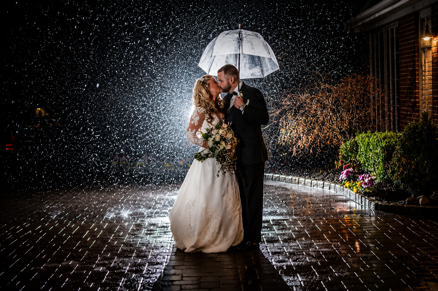 Bride and groom kissing under an umbrella in a rainy outdoor wedding scene