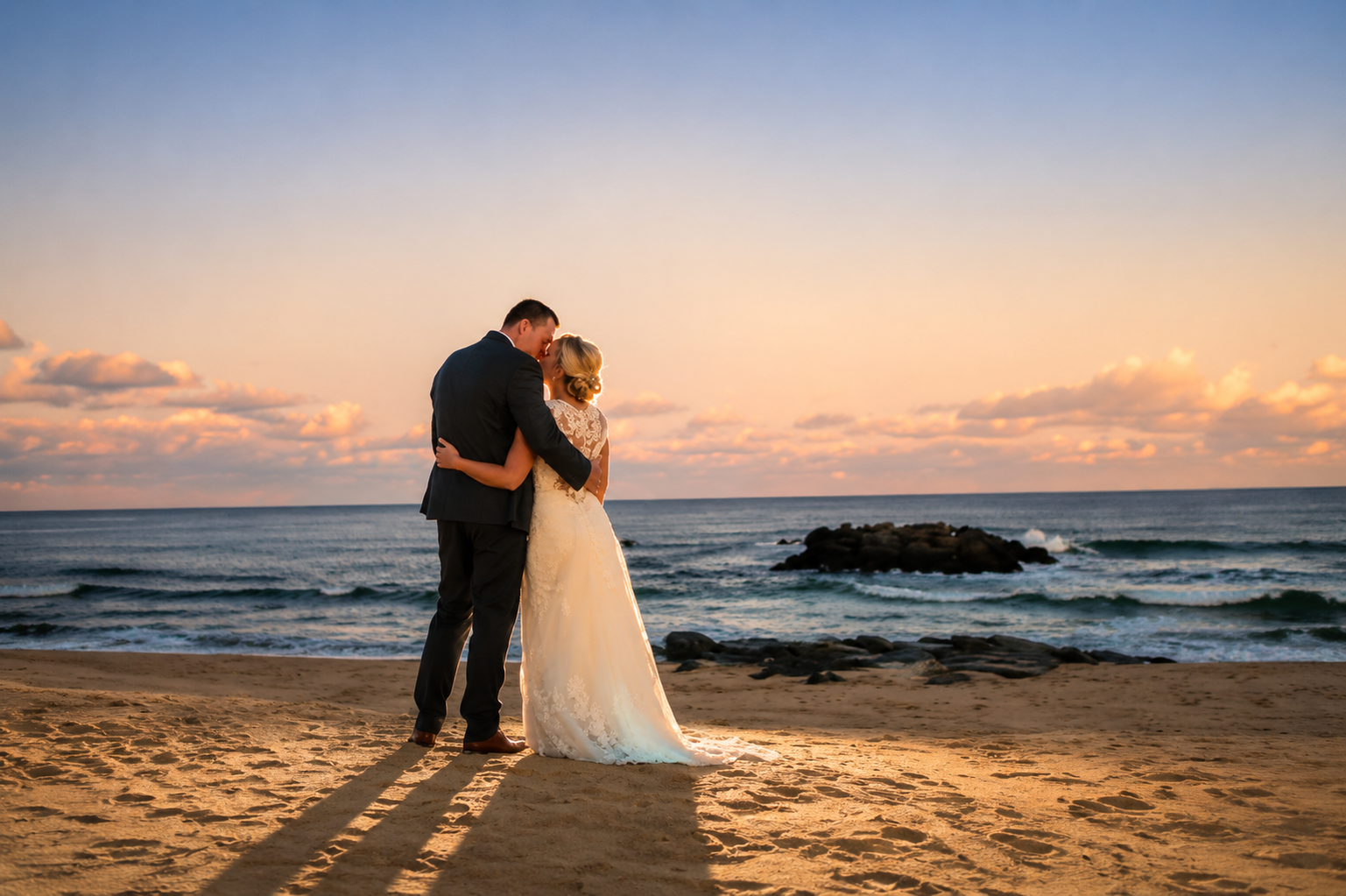 Couple embracing on a beach at sunset with waves and rocky shoreline behind them