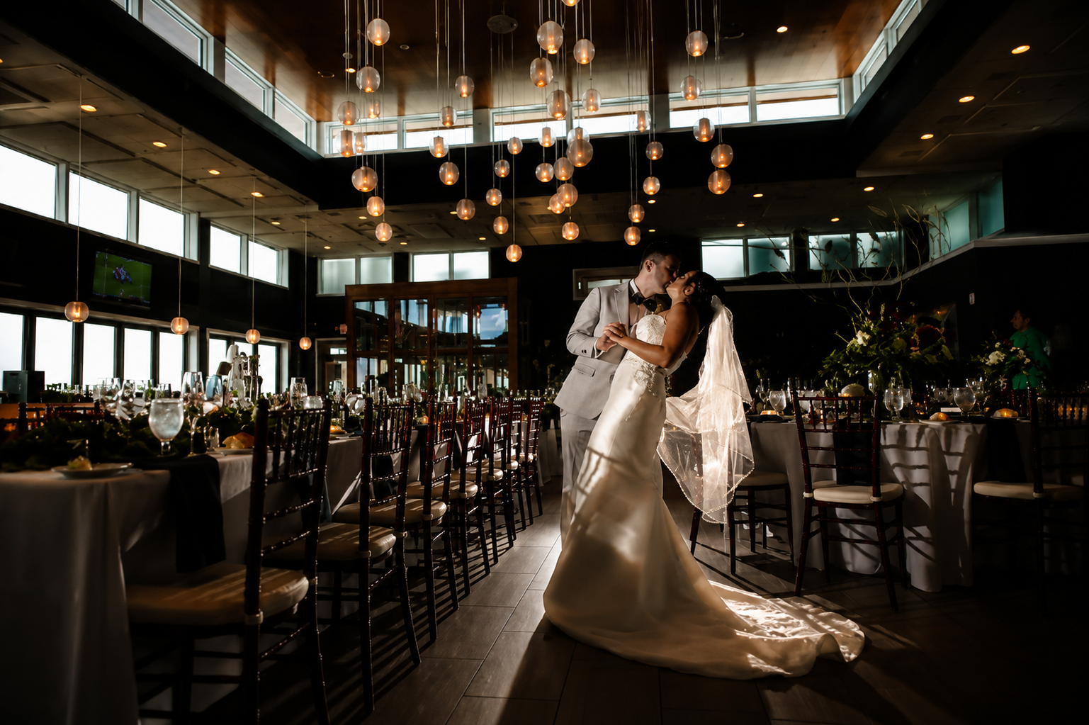 Bride and groom kissing in a dimly lit reception hall under hanging lights