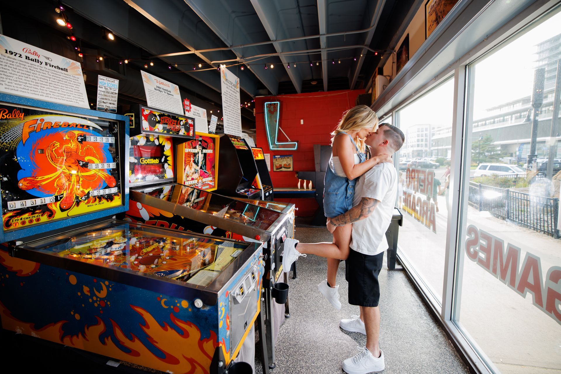 Person hugging a child inside a brightly lit arcade beside colorful game machines and large windows