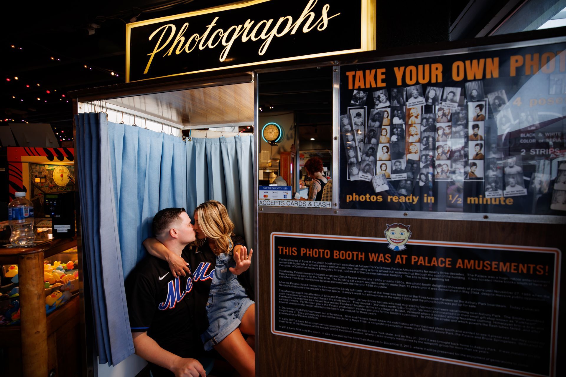 Couple kissing in a vintage photo booth beside a “Take Your Own Picture” sign