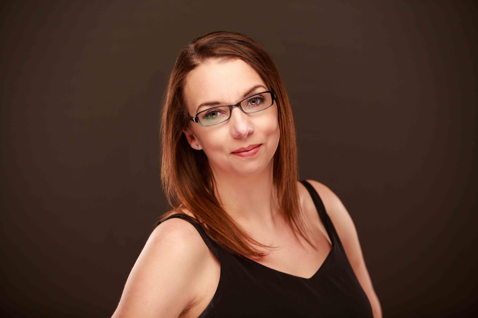Portrait of a woman with glasses and brown hair against a dark studio background