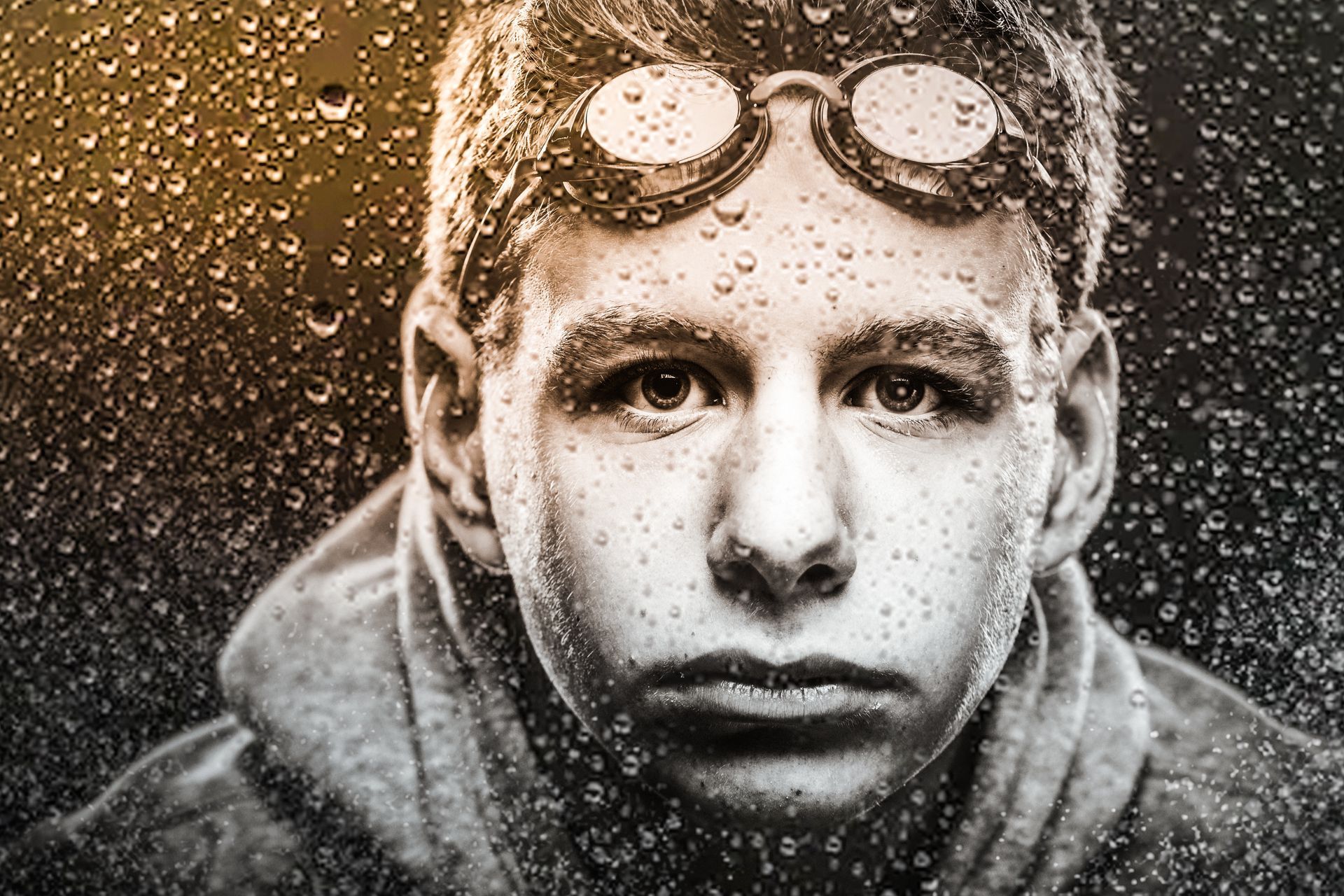 Close-up of a person wearing goggles, with water droplets splashing across their face and jacket.