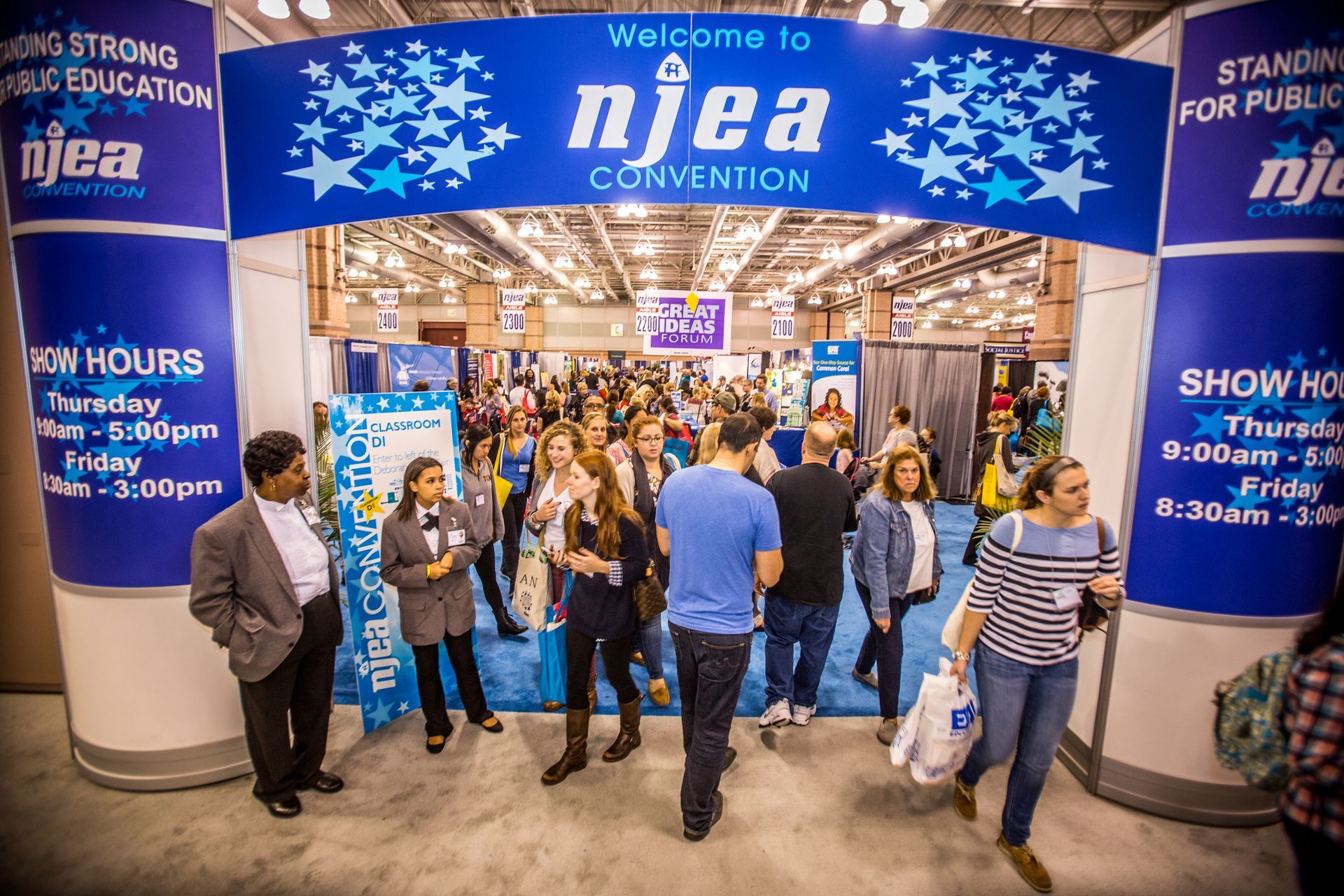 Convention entrance with blue NAEA banner, people gathered inside, and “Show Hours” signs on the pillars