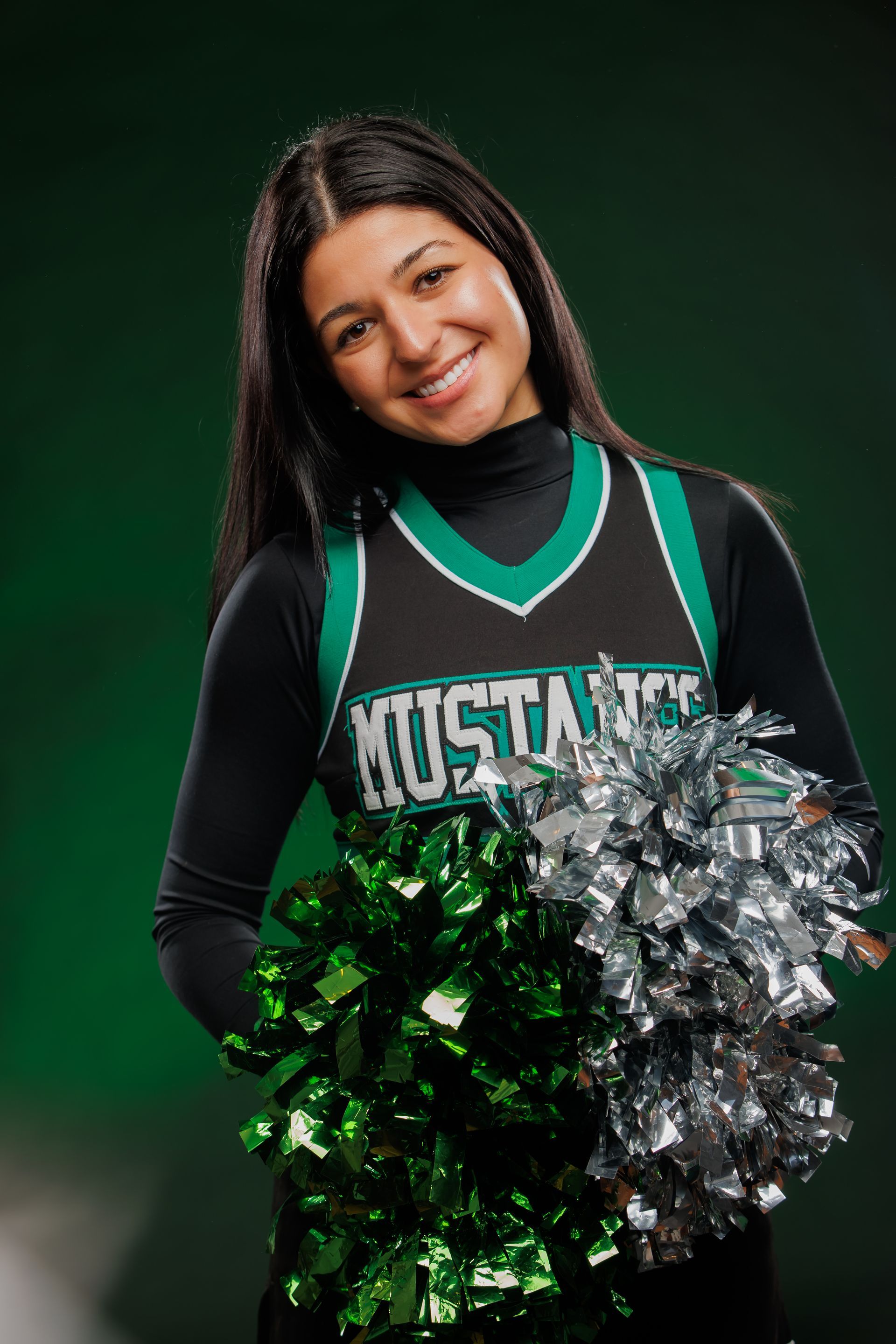 Cheerleader in green-and-black uniform holding green and silver pom-poms against a dark background