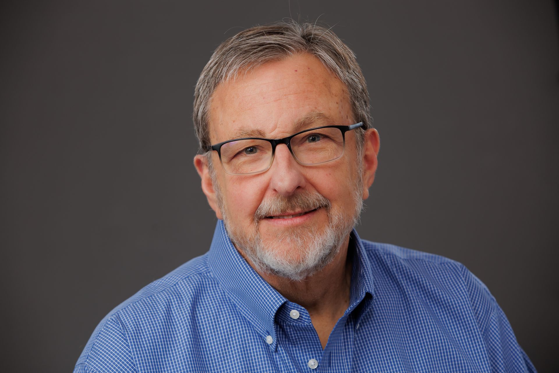 Portrait of a smiling man in glasses and a blue striped shirt against a gray background