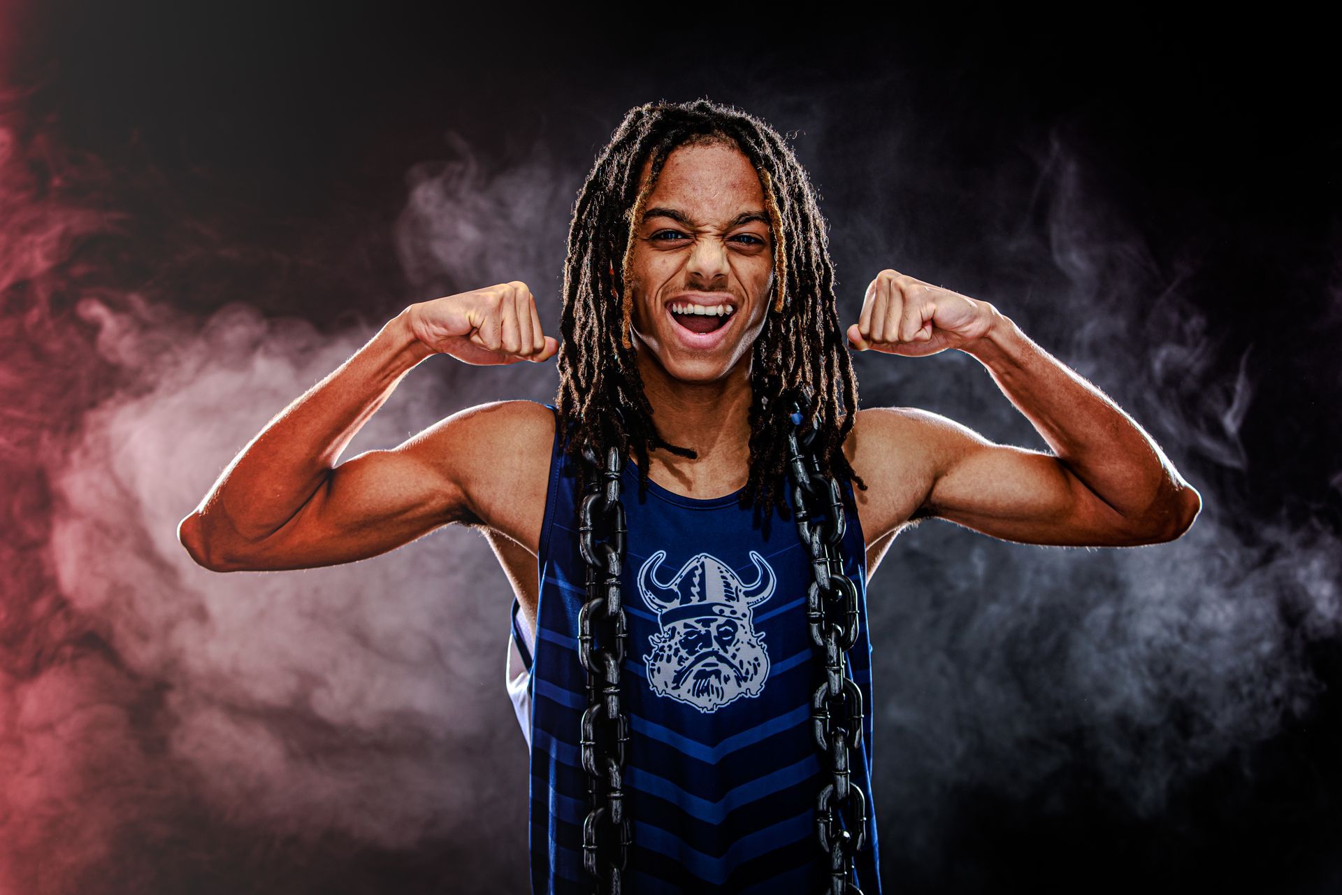 Smiling person flexing both arms in a blue shirt against a smoky dark background
