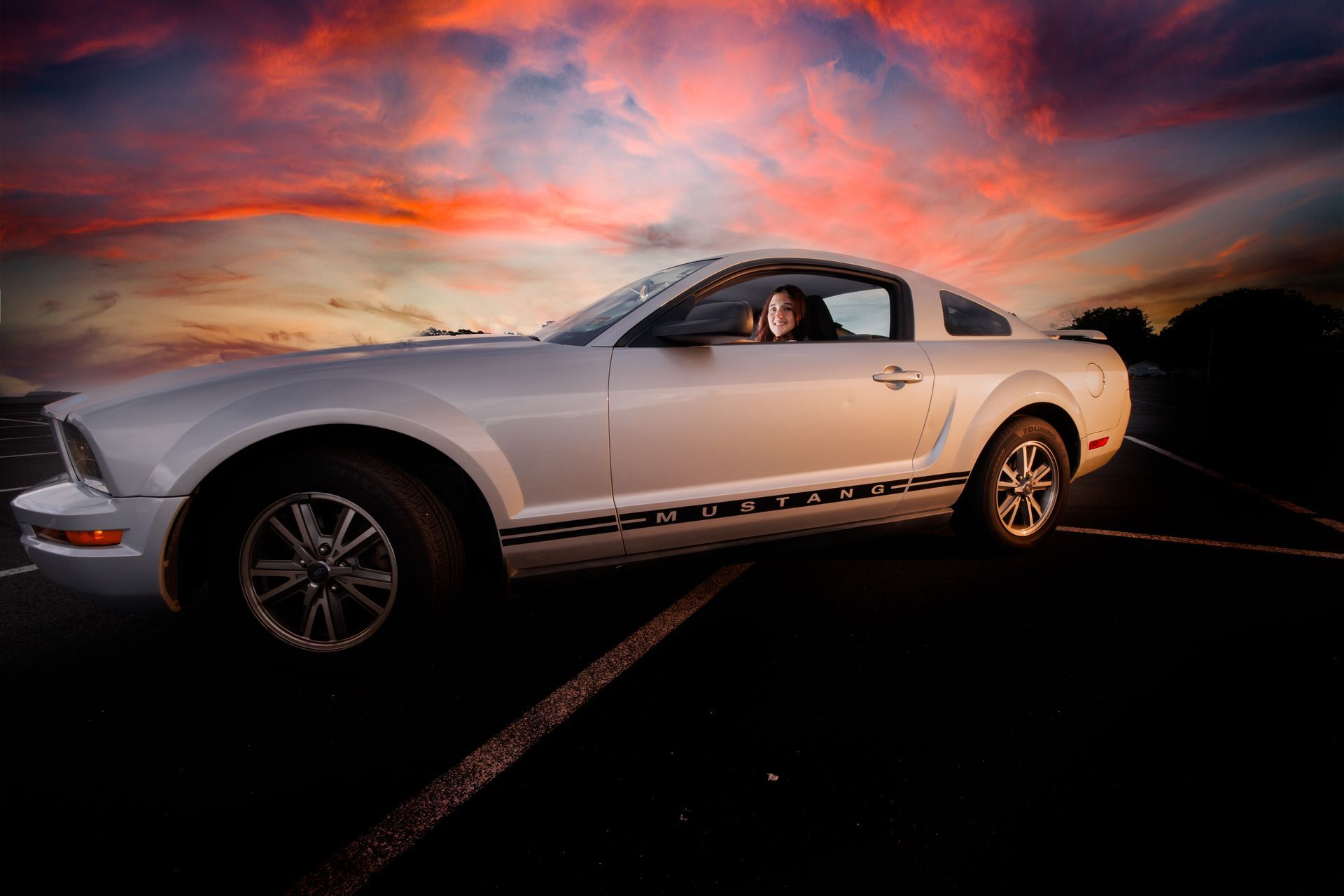 White sports car with driver at sunset on a road, under a colorful sky