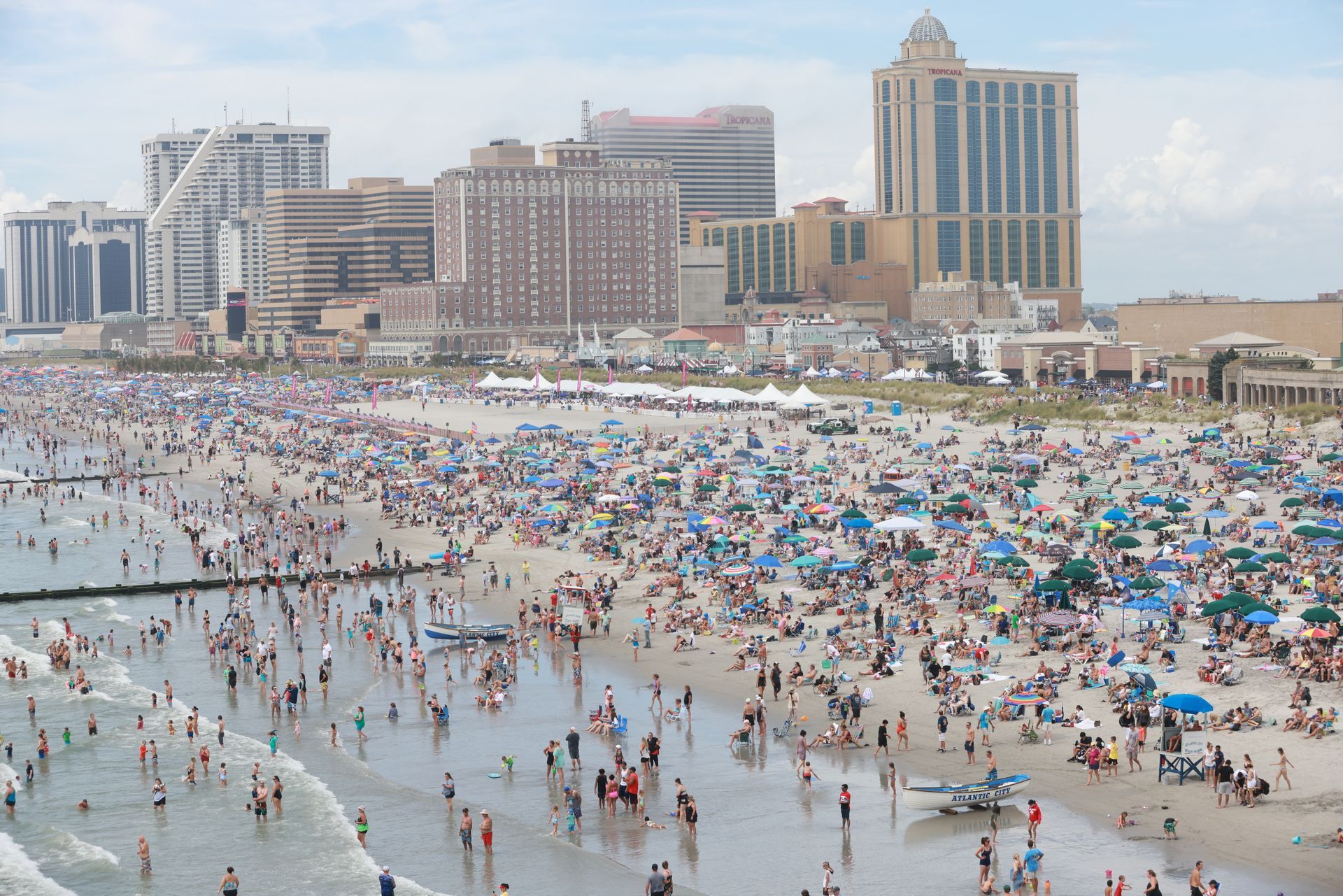Crowded beach with umbrellas and swimmers beside a coastal skyline of tall hotels and condos