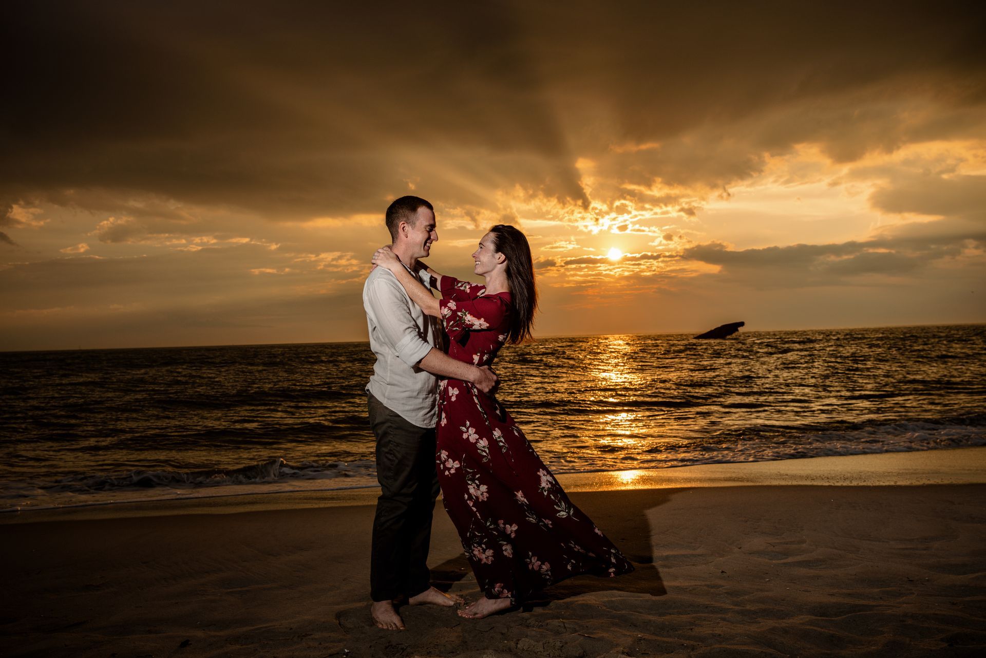 Couple embracing on a beach at sunset, silhouetted against glowing ocean and sky.