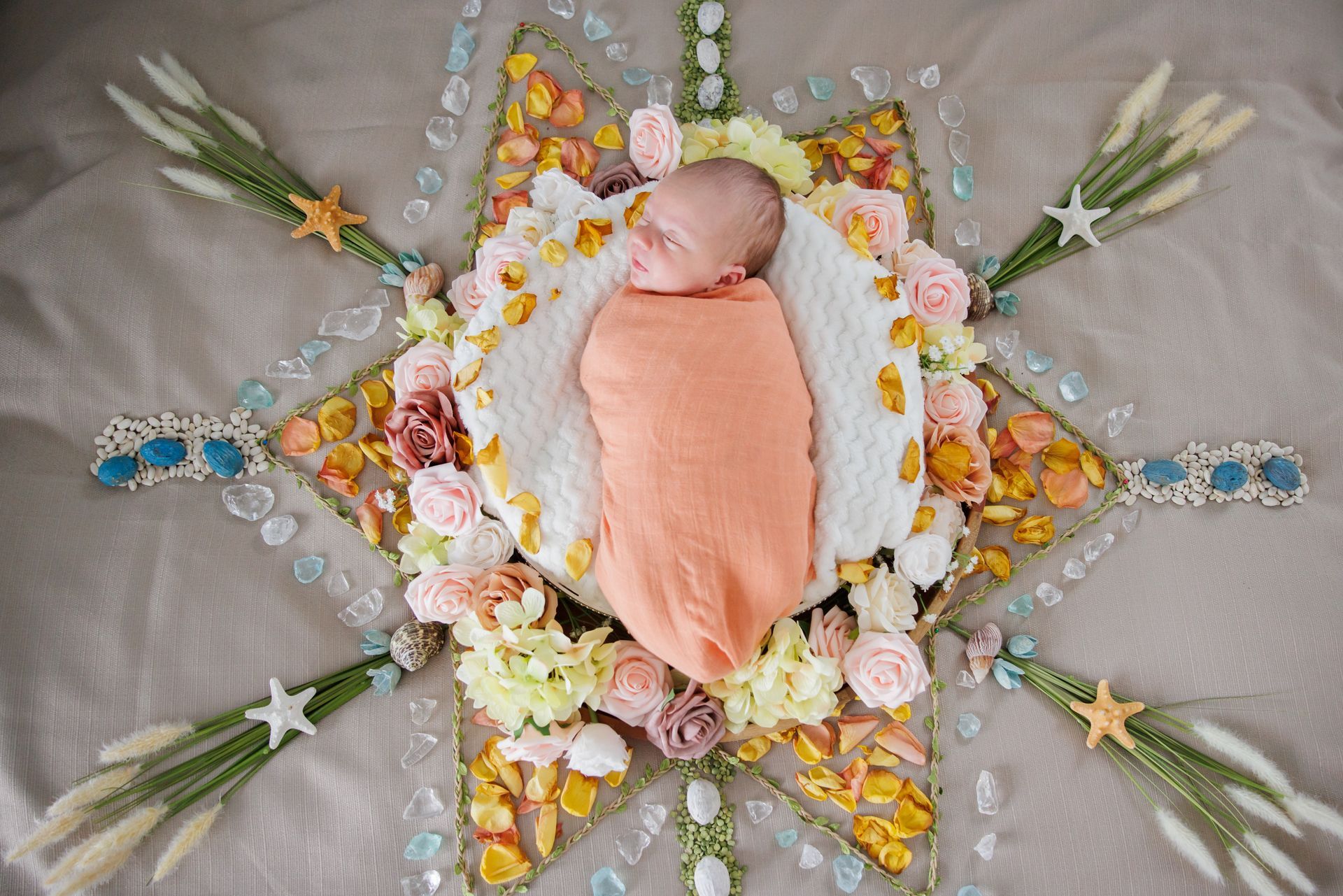Infant in peach swaddle on floral, star-shaped blanket arrangement