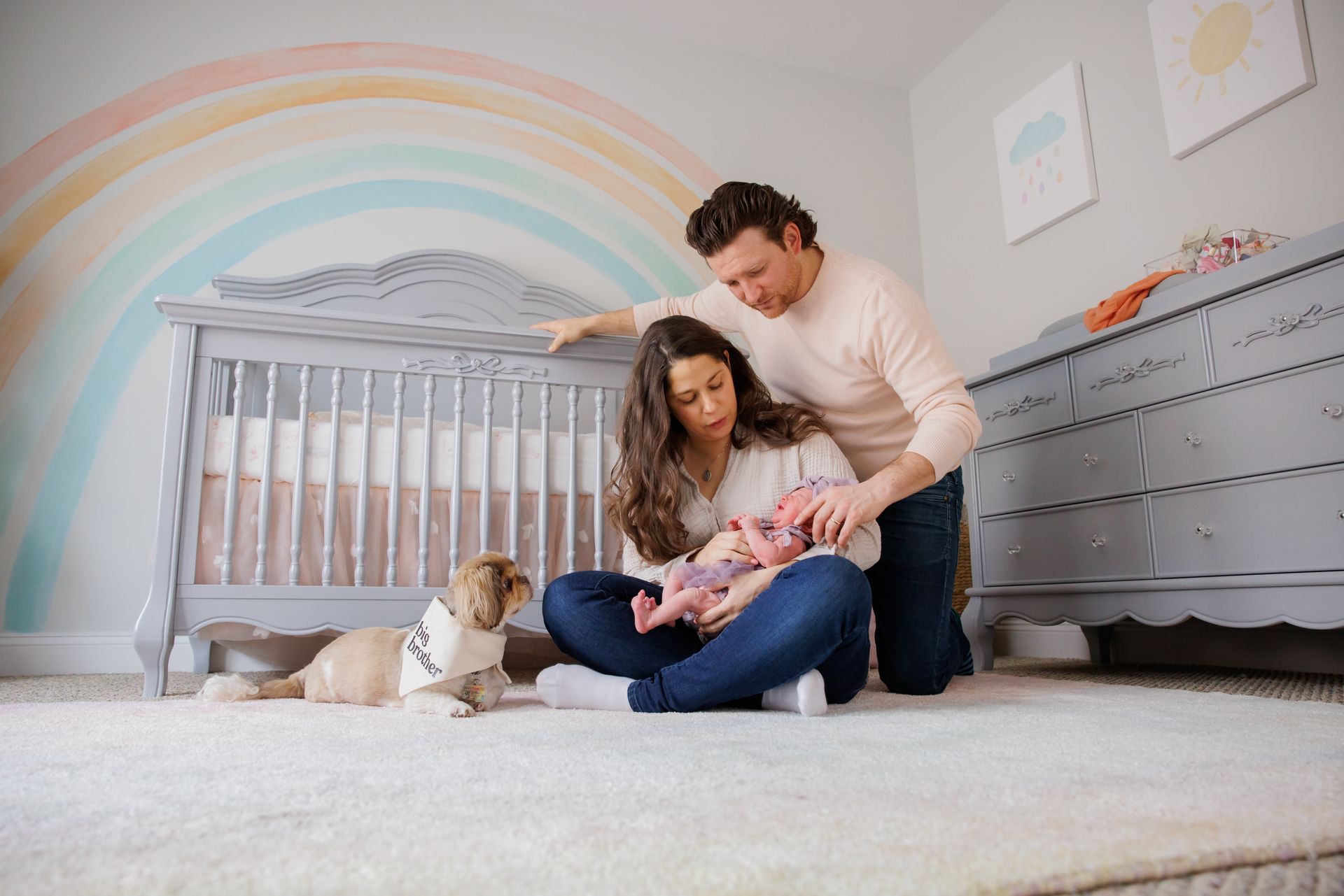 Parents reading to baby in a nursery with a rainbow mural and a crib