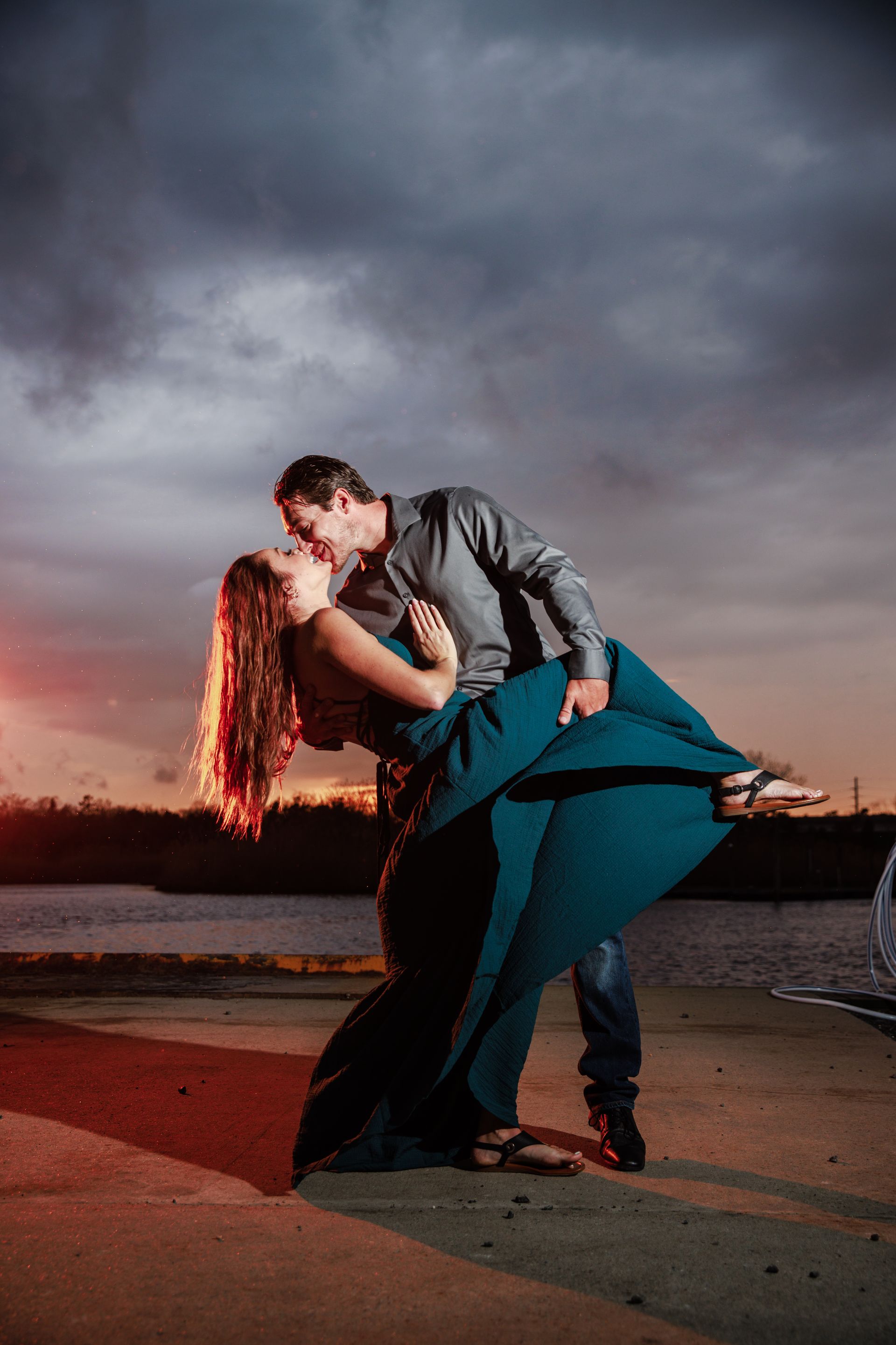 Couple embracing and kissing on a waterfront at dusk under a cloudy sky