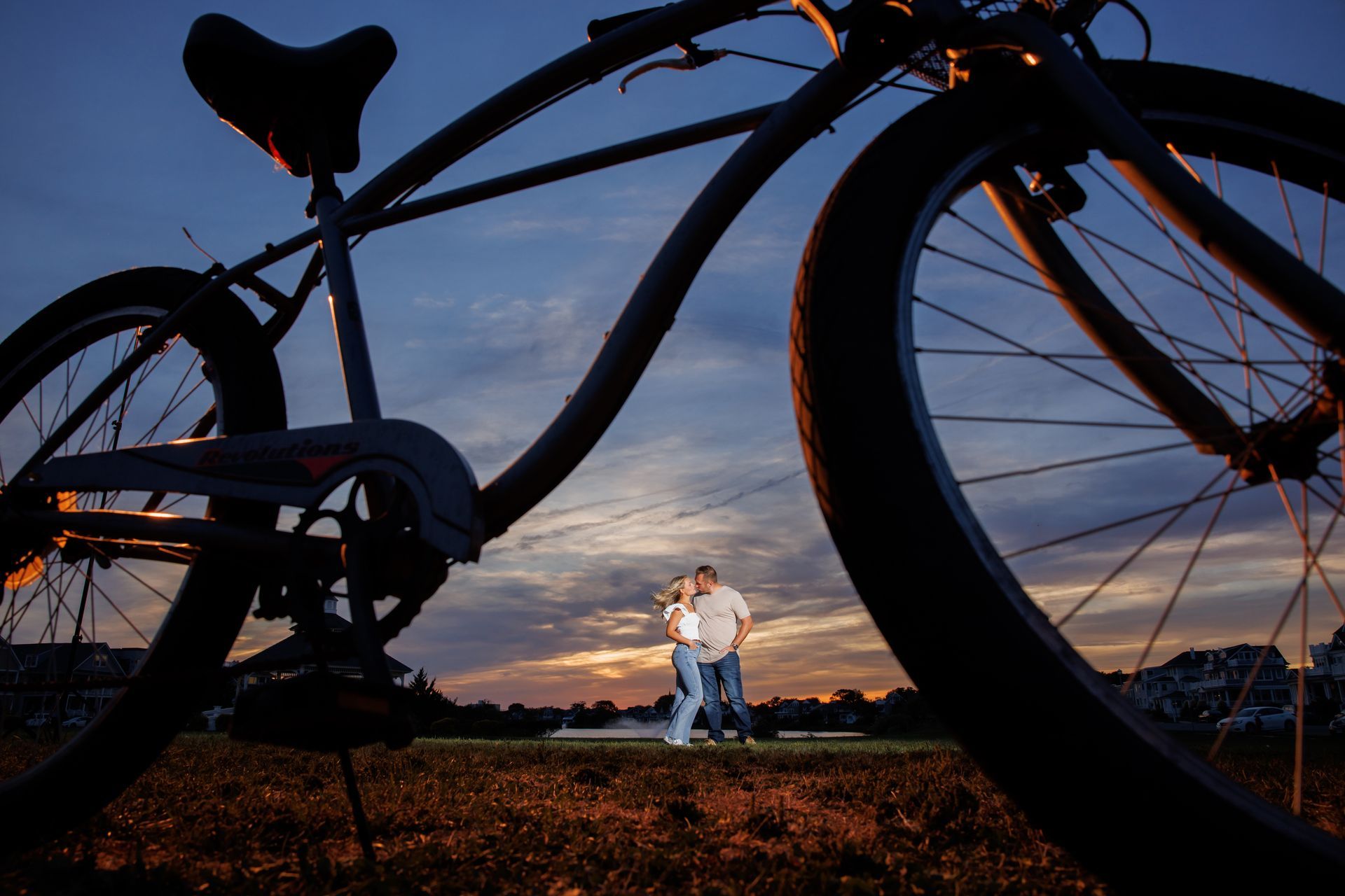 Silhouetted bicycle against a sunset sky, with a couple standing in the field behind it
