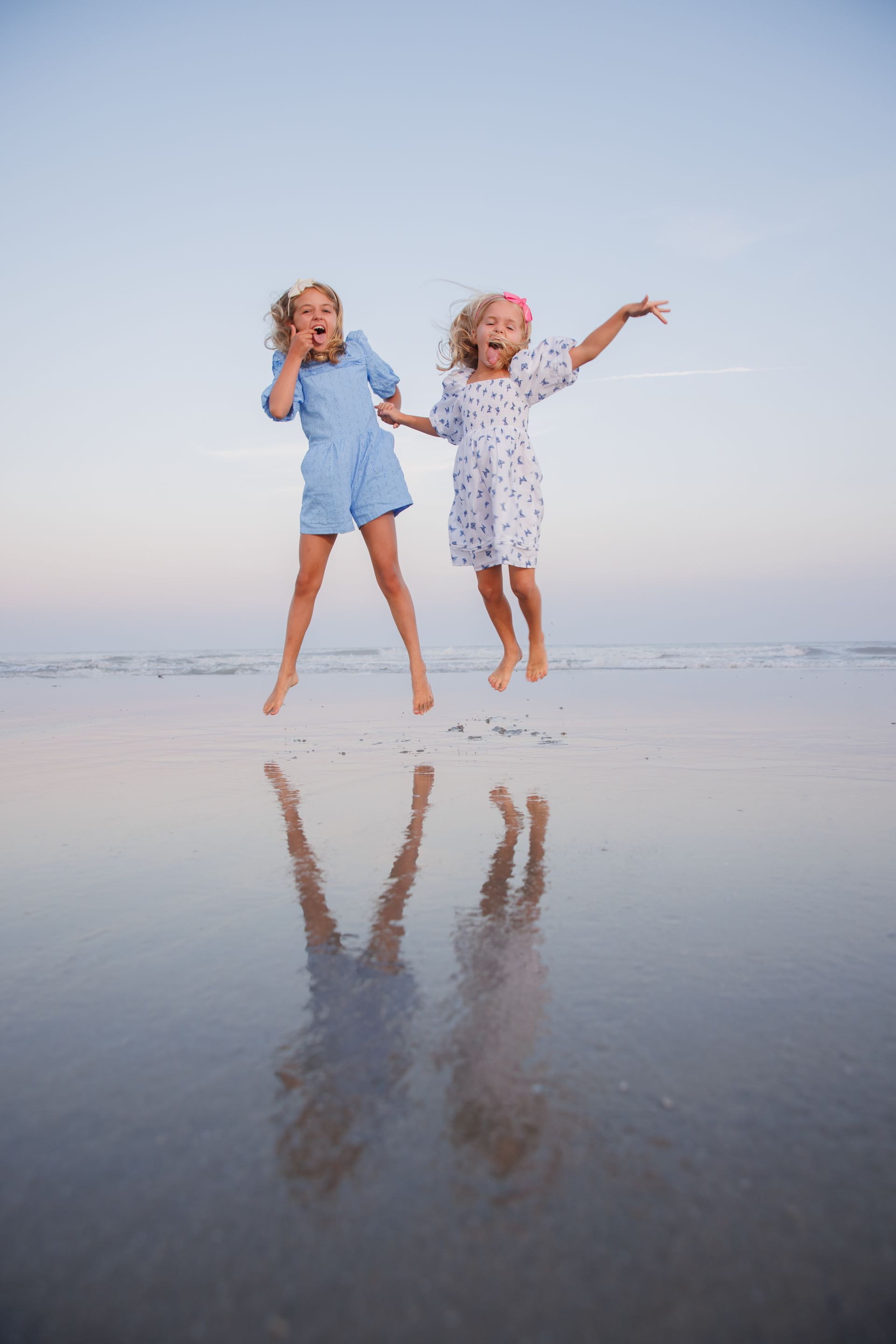Two people jumping on a wet beach at sunset, with their reflections in the water.