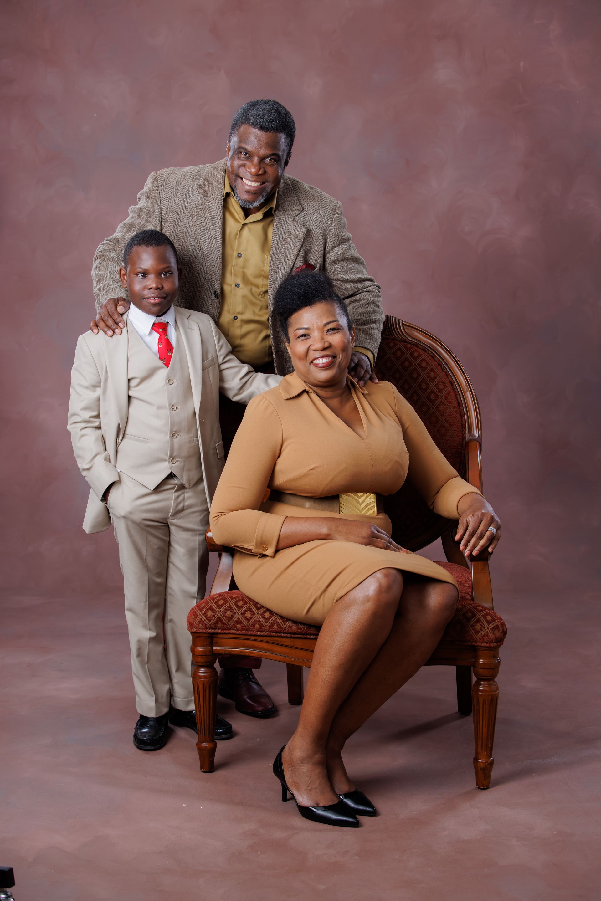 Formal family portrait with a seated woman, standing man, and child against a plain studio backdrop.